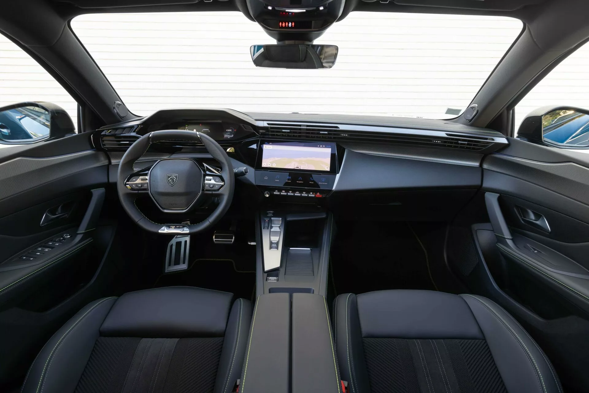 Vista interior del Peugeot 408 2023 desde los asientos traseros destacando el tablero de mandos, el volante multifunción con emblema de la marca y el sistema de infoentretenimiento avanzado