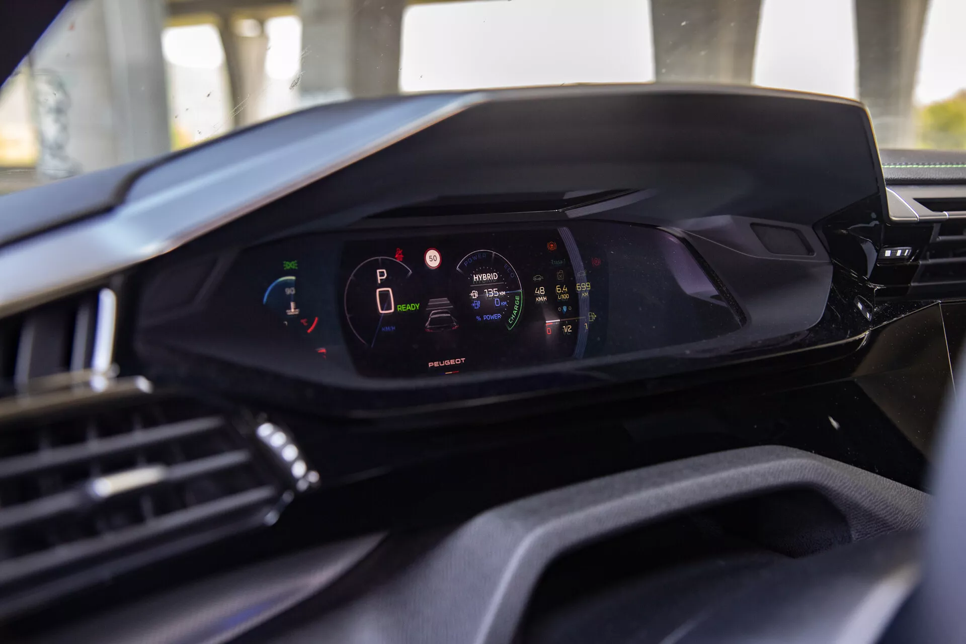 Vista interior del Peugeot 408 2023 destacando el tablero digital moderno desde la perspectiva del asiento del conductor, mostrando el cuadro de instrumentos digital con el vehículo en modo estacionamiento y nivel alto de carga de batería