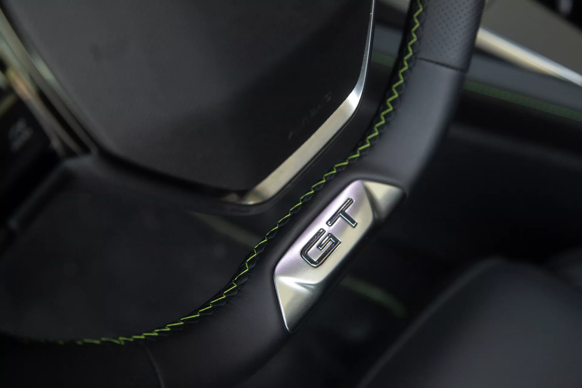 Vista detallada del volante y sección del tablero del Peugeot 408 2023, mostrando un volante de cuero negro con costuras verdes y una insignia GT, resaltando lujo y deportividad