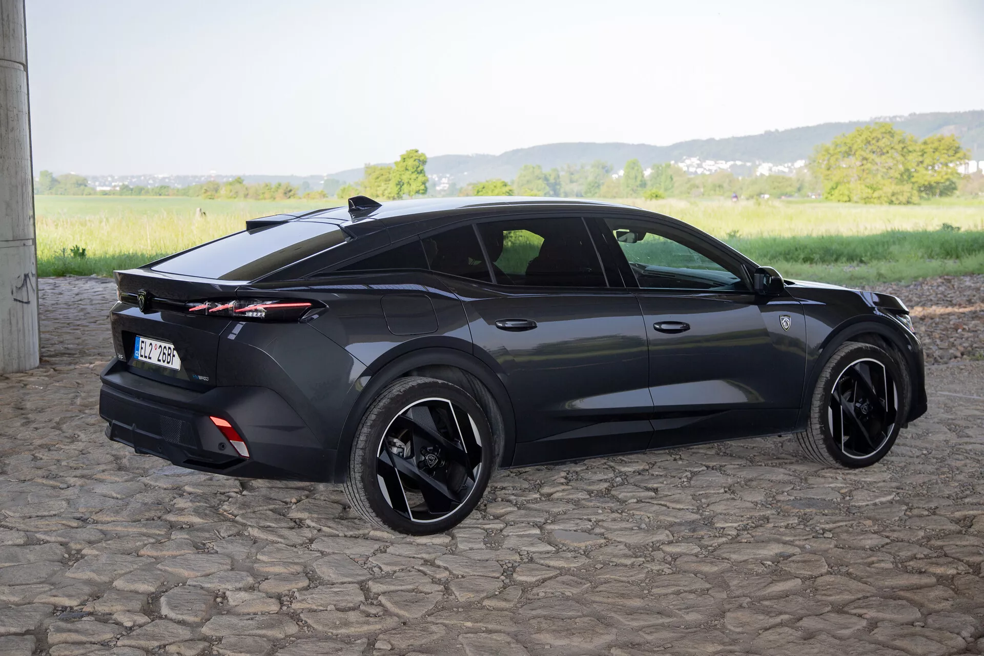 Peugeot 408 de 2023 captado desde un ángulo trasero de tres cuartos que resalta su diseño deportivo tipo hatchback, spoiler trasero integrado con luces traseras de longitud completa, ruedas de aleación negras y características contemporáneas como manijas de puertas al ras y espejos laterales con señales de giro, en luz natural del día