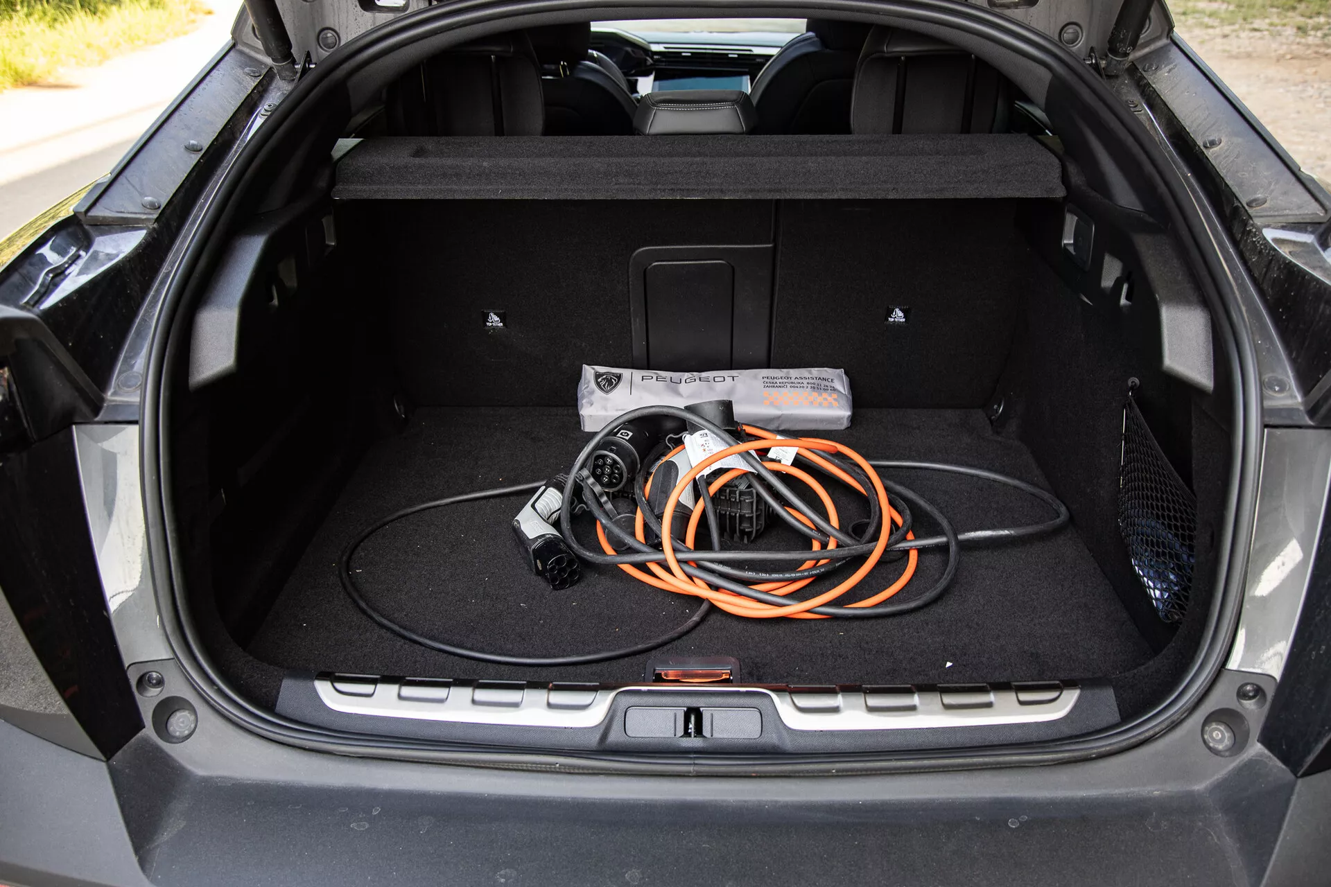 Vista interior del maletero del Peugeot 408 2023 mostrando un diseño espacioso y un cable de carga para vehículos eléctricos, destacando la tecnología EV y la calidad de construcción moderna.