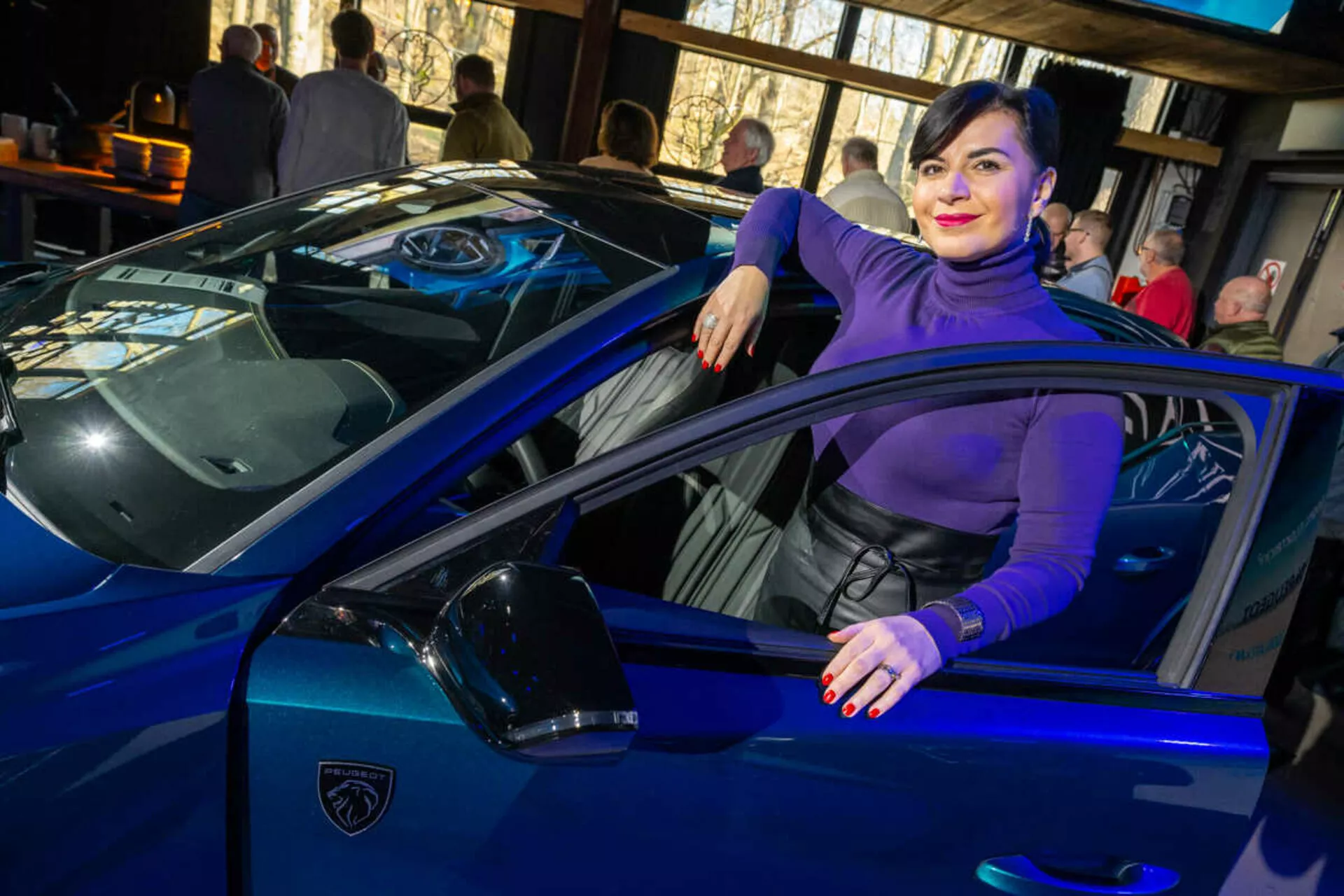Coche deportivo azul vibrante, posiblemente un Lamborghini, capturado desde un ángulo de tres cuartos enfatizando sus líneas elegantes, faros LED afilados e icónico logo en forma de escudo, con una persona interactuando casualmente con el vehículo insinuando lujo y estilo.