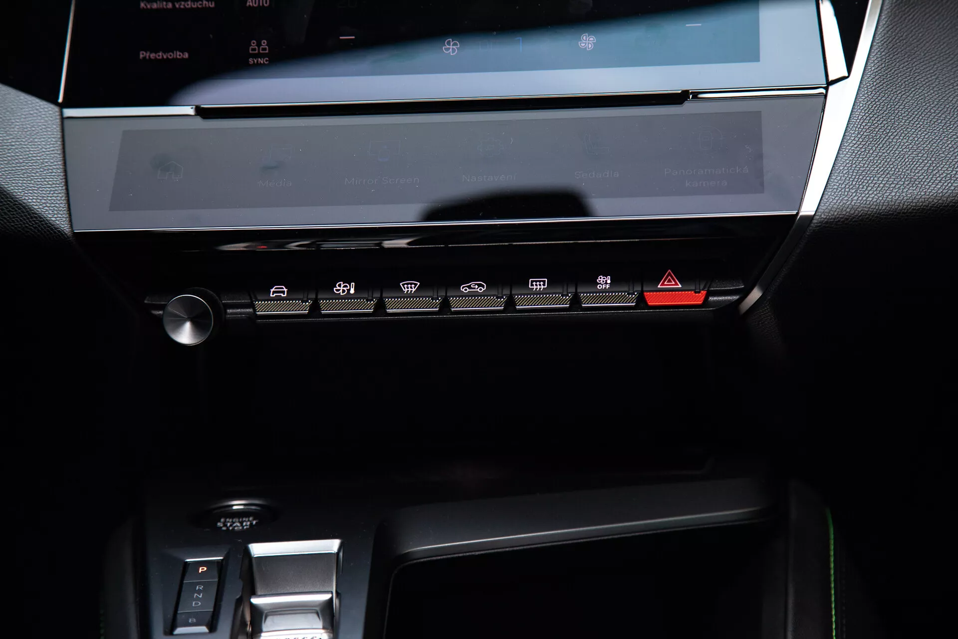 Tablero central de un Peugeot 408 2023 mostrando la pantalla táctil del sistema de infoentretenimiento apagada, panel de control climático con botones sensibles al tacto y parte del área de cambio de marchas electrónico, bajo una suave iluminación ambiental que resalta su diseño moderno y elegante con tonos oscuros y detalles metálicos.