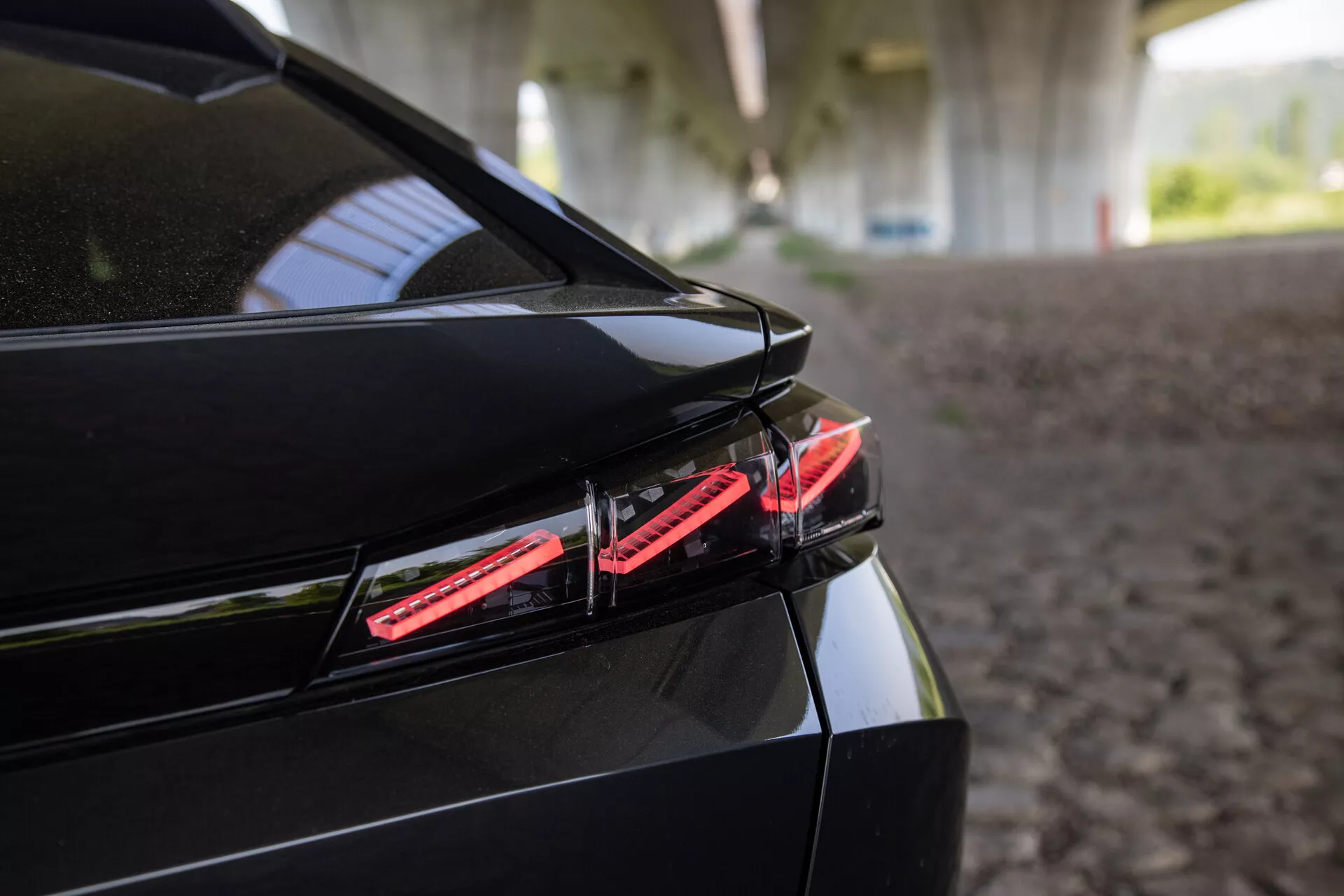 Primer plano de la parte trasera del Peugeot 408 de 2023 mostrando la luz trasera LED, el diseño elegante del maletero con spoiler integrado y el acabado negro brillante bajo una sombra estructurada