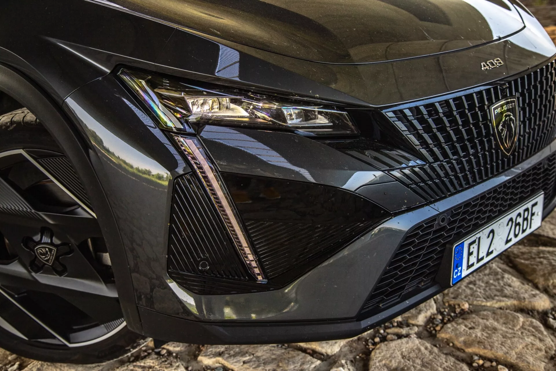 Vista de cerca de la esquina frontal izquierda del Peugeot 408 2023 mostrando el conjunto detallado del faro, sección de la parrilla, capó y rueda con tecnología LED moderna y elementos de diseño de lujo.
