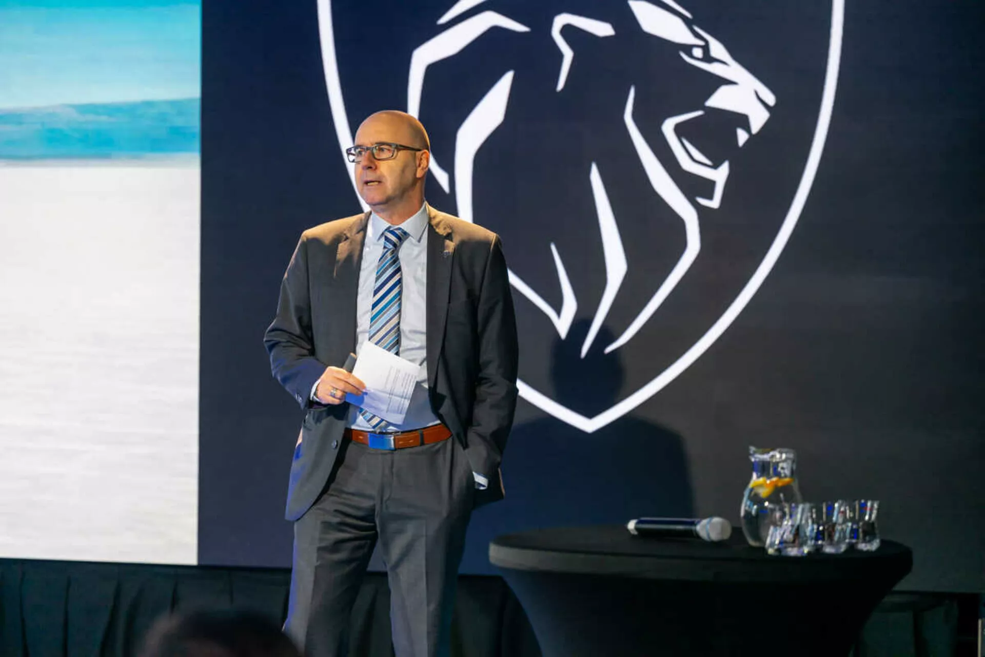 Orador profesional presentando frente a un fondo con un logo de cabeza de tigre, posiblemente representando una marca, ningún Peugeot 408 o auto visible