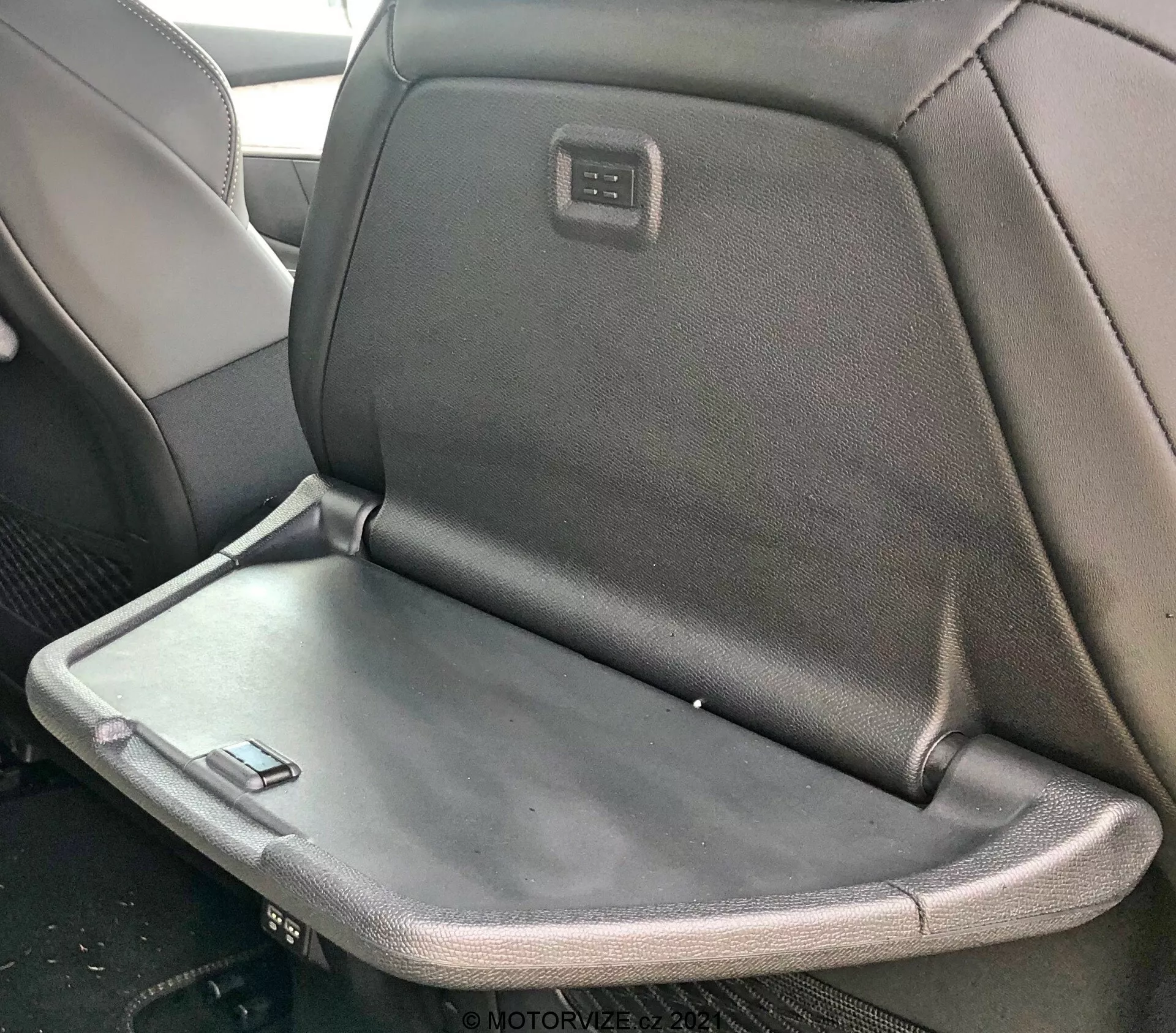 Vista interior de un Peugeot 5008 2021 con un asiento trasero que presenta un reposabrazos plegable o mesa bandeja, mostrando una mezcla de tapicería en tela y cuero con una pantalla integrada o panel de control en la parte trasera del reposacabezas del asiento delantero.