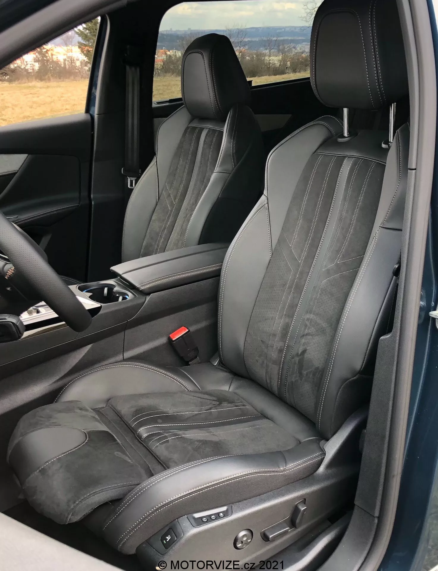 Vista interior del Peugeot 5008 2021 centrada en el asiento del conductor, mostrando un asiento de cuero negro ajustable con costuras contrastantes y grabado horizontal, tomada desde una perspectiva de puerta abierta, destacando el diseño ergonómico y de lujo con controles electrónicos de ajuste de asiento y una parte de la consola central y el volante visible.