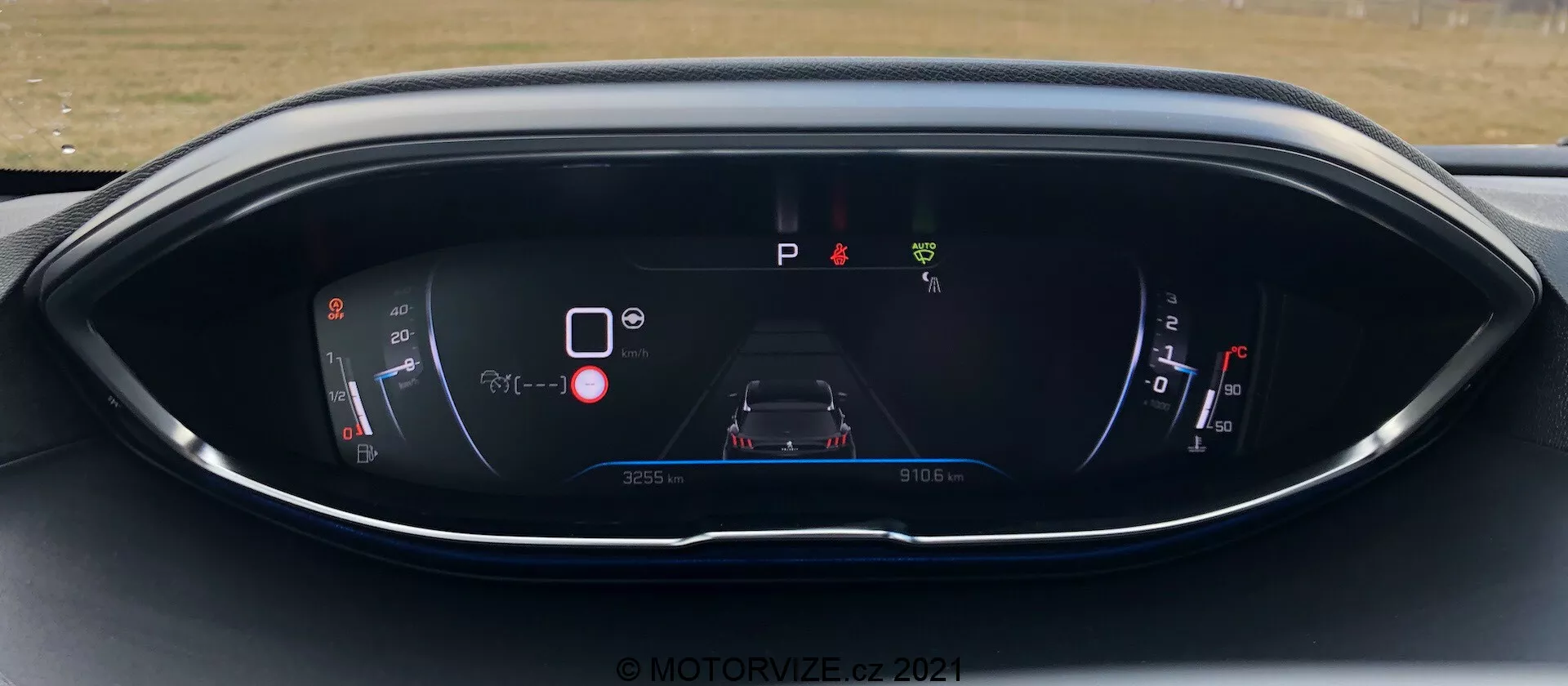 Tablero de instrumentos del Peugeot 5008 2021, mostrando una pantalla digital desde la perspectiva del conductor. La pantalla incluye un indicador de potencia/batería, un gráfico central del automóvil con íconos de advertencia, un indicador de 'P' de estacionamiento, un indicador de combustible y la información del cuentakilómetros/viaje. El diseño presenta un esquema de colores moderno azul y rojo en una carcasa curva y elegante. Marca de agua © MOTOR1ZED 2021.