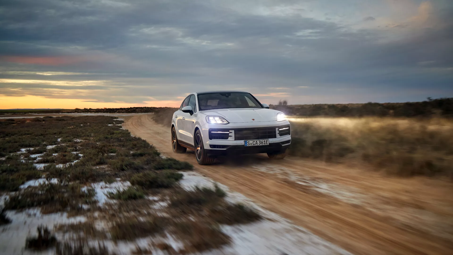 Modelo 2023 Porsche Cayenne 9YA Facelift conduciendo fuera de carretera, mostrando su vista frontal de tres cuartos con faros LED, suspensión activa y sistema de tracción total en un entorno de crepúsculo