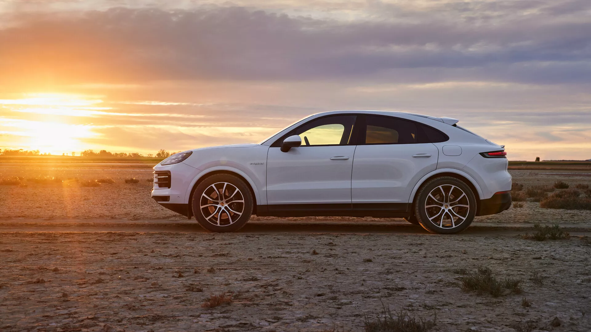 SUV crossover de lujo Porsche Cayenne 2023 en blanco brillante sobre terreno árido a la hora dorada, mostrando vista de perfil, ruedas de aleación deportivas y elegantes características de diseño