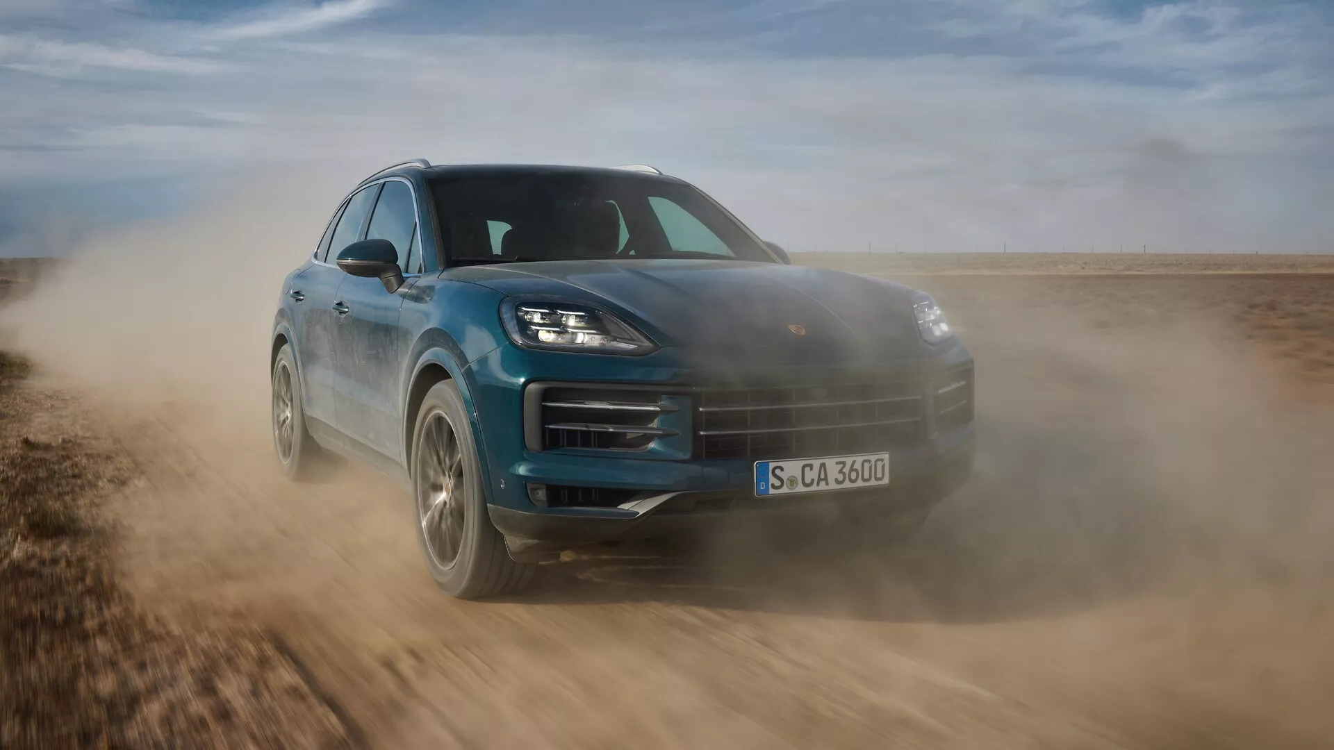 Porsche Cayenne 2023 (facelift 9YA) en movimiento dinámico, mostrando su diseño elegante y capacidades fuera de carretera, capturado desde un ángulo frontal bajo de tres cuartos que destaca la postura deportiva, faros LED avanzados y características aerodinámicas en una superficie no pavimentada.