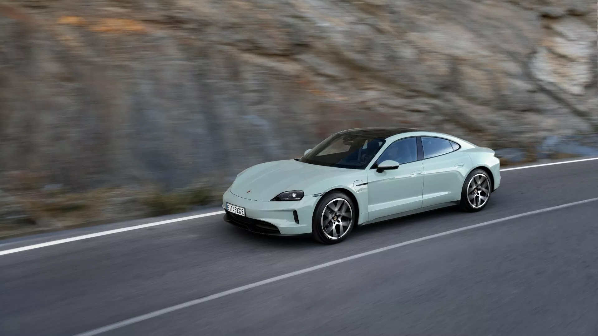 Porsche Taycan Y1A restyling 2024 en movimiento en una carretera de montaña, destacando su diseño aerodinámico tipo coupé, faros LED y postura deportiva