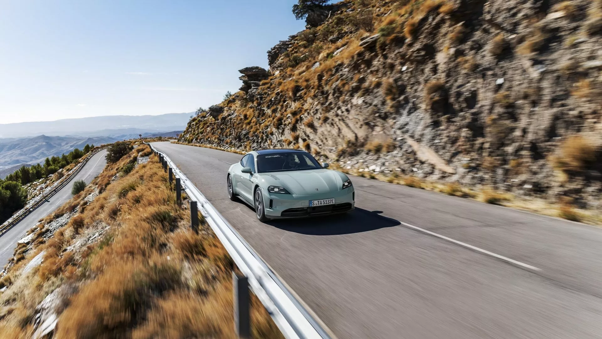 Porsche Taycan 2024 (Y1A Facelift) en movimiento en una carretera montañosa mostrando diseño aerodinámico, faros LED y llantas deportivas