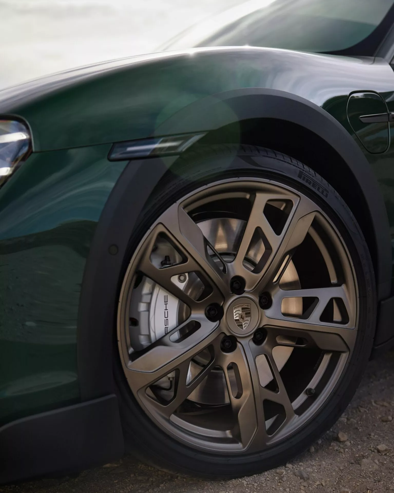 Vista detallada de la rueda delantera de un coche de alto rendimiento de lujo que muestra un diseño de aleación de bronce multipalas, neumático de bajo perfil, disco de freno perforado avanzado y pinza de tamaño considerable contra un trabajo de carrocería oscuro elegante, con un atisbo del sistema de iluminación moderno.
