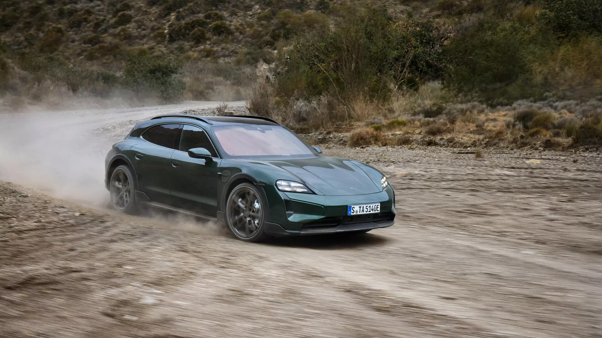 Vista dinámica del Porsche Taycan 2024 (restyling Y1A) en movimiento sobre un camino no pavimentado, destacando sus faros LED, diseño aerodinámico, ruedas de aleación y estela de polvo indicativa de alta velocidad y capacidades de tracción integral.