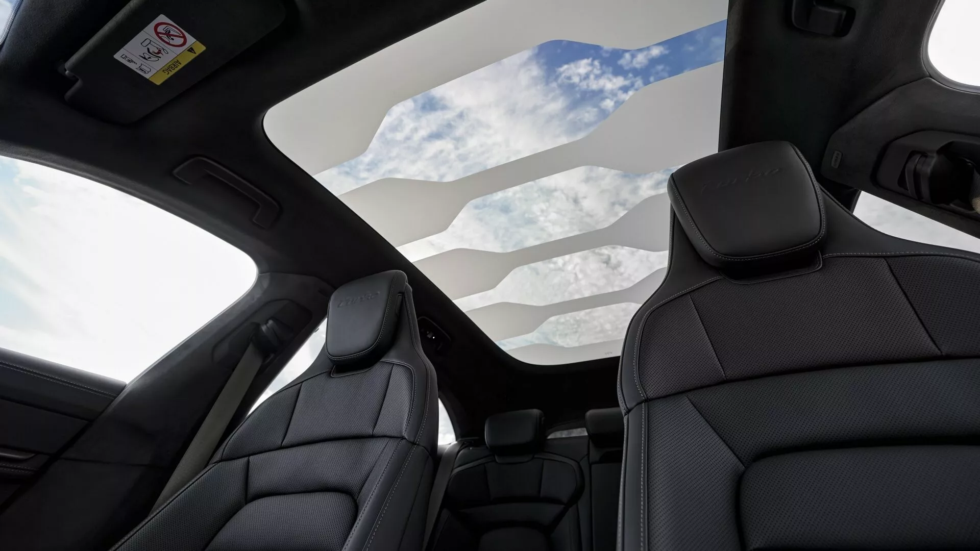Vista interior de un Porsche Taycan 2024 con techo solar panorámico y asientos de cuero negro premium, destacando características de lujo y tecnologías de seguridad