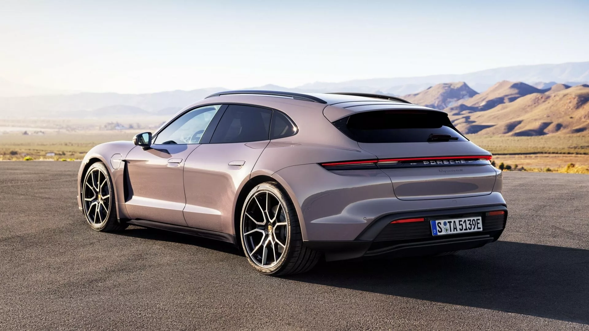 Vista trasera de tres cuartos del Porsche Taycan 2024 (Y1A Facelift) mostrando su perfil aerodinámico, techo panorámico, luces traseras horizontales delgadas, difusor trasero, grandes ruedas de aleación de múltiples radios, manijas de puerta al ras y acabado mate