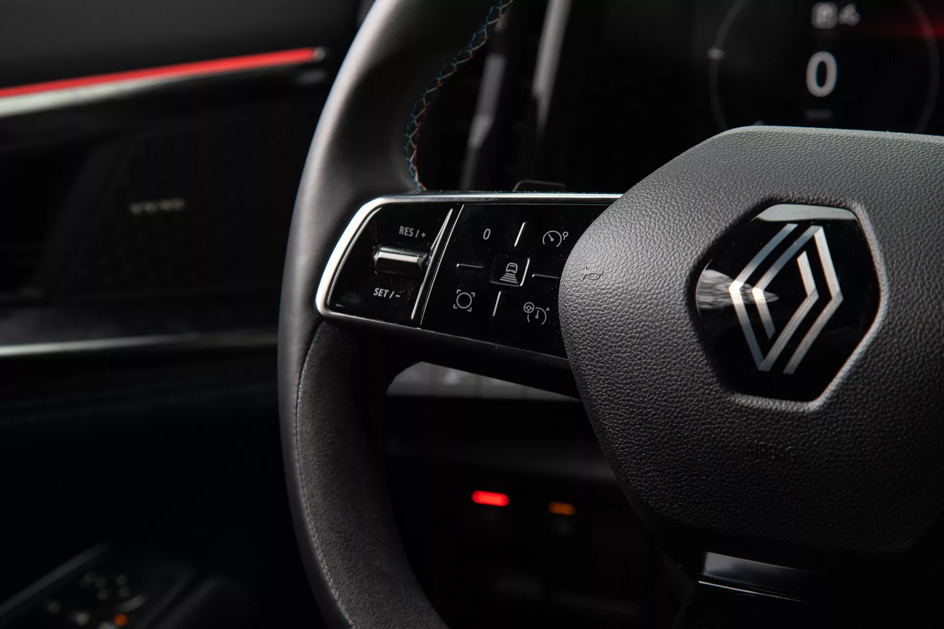 Vista interior del Renault Austral 2022 destacando los controles del volante y el emblema, incluyendo funciones de botón iluminado para volumen, llamadas, comandos de voz y navegación de infotenimiento, desde la perspectiva del asiento del conductor.