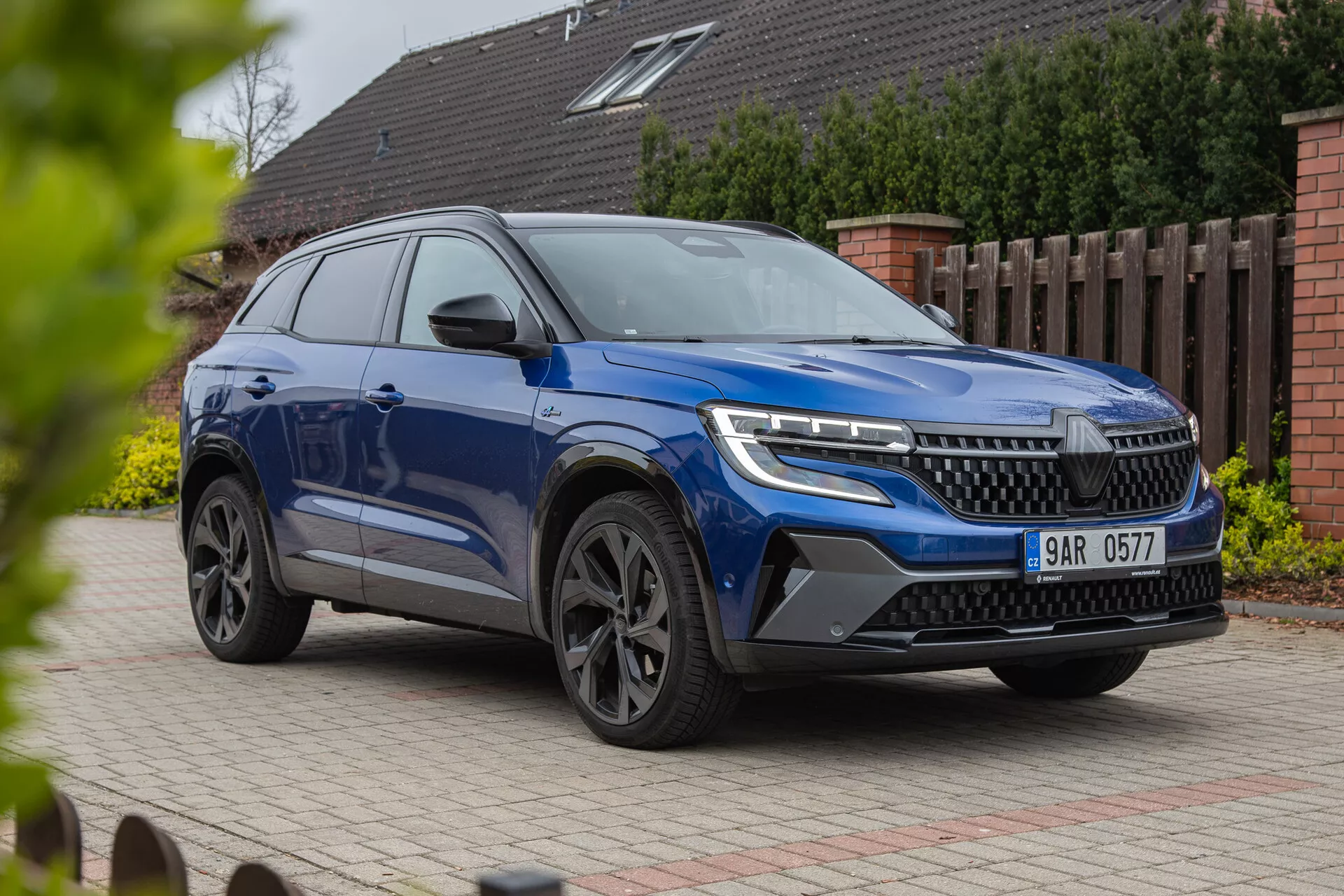 SUV moderno Renault Austral 2022 mostrado desde una perspectiva frontal de tres cuartos destacando faros LED, una parrilla prominente, ruedas de aleación estilosas y carrocería dinámica con acabado de pintura metálica, fotografiado desde un ángulo bajo para enfatizar su estatura y características de diseño contra un fondo residencial.