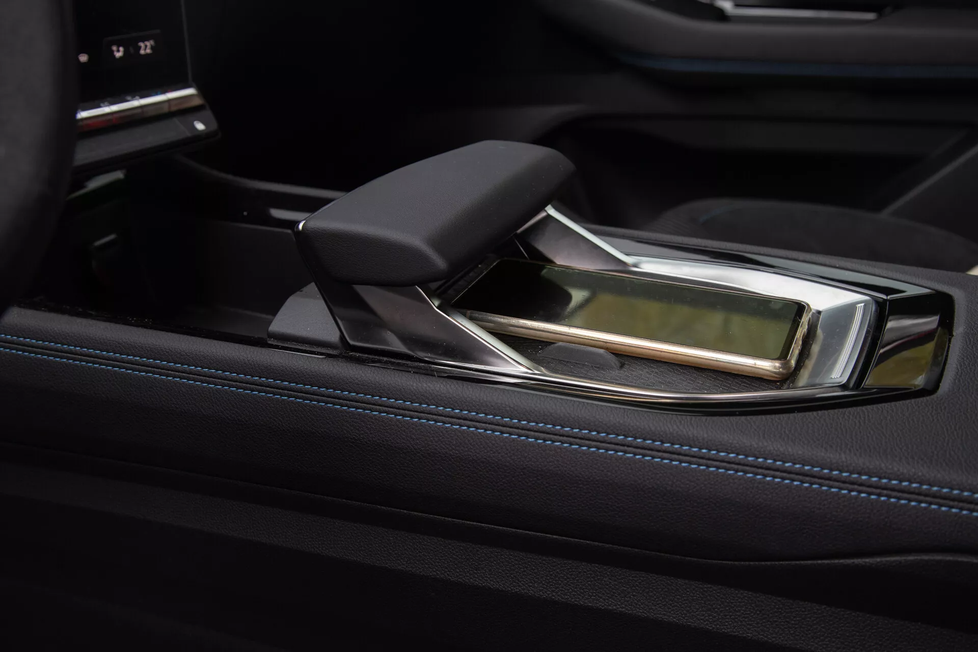 Vista detallada de la consola central lujosa del Renault Austral 2022 con una palanca de cambios automática moderna, presentando un diseño ergonómico con detalles en cuero y cromo, contra un fondo de acabado negro brillante y un sofisticado interfaz de control de entretenimiento.