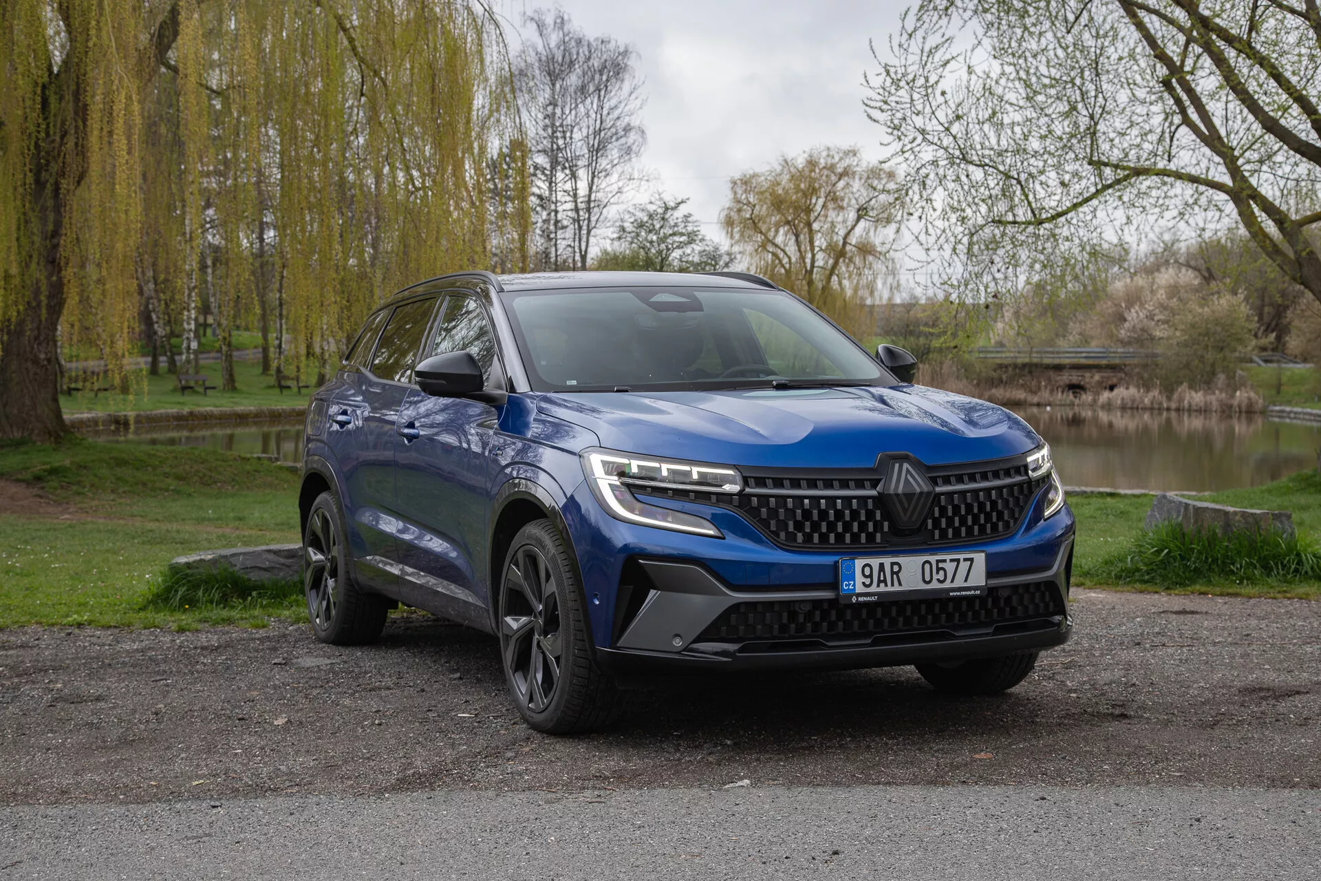 SUV azul Renault Austral 2022 estacionado al aire libre mostrando la fascia frontal y el lado del conductor con faros LED, paragolpes deportivo y llantas de aleación contra un telón de fondo natural