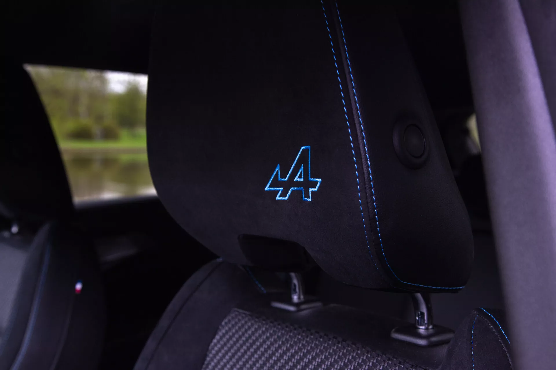Vista detallada del interior del Renault Austral 2022 mostrando el asiento del conductor de tela negra con costuras azules distintivas y un logotipo estilizado 'A' en el reposacabezas, guía integrada para el cinturón de seguridad visible, sugiriendo características de vehículo moderno y posiblemente deportivo.