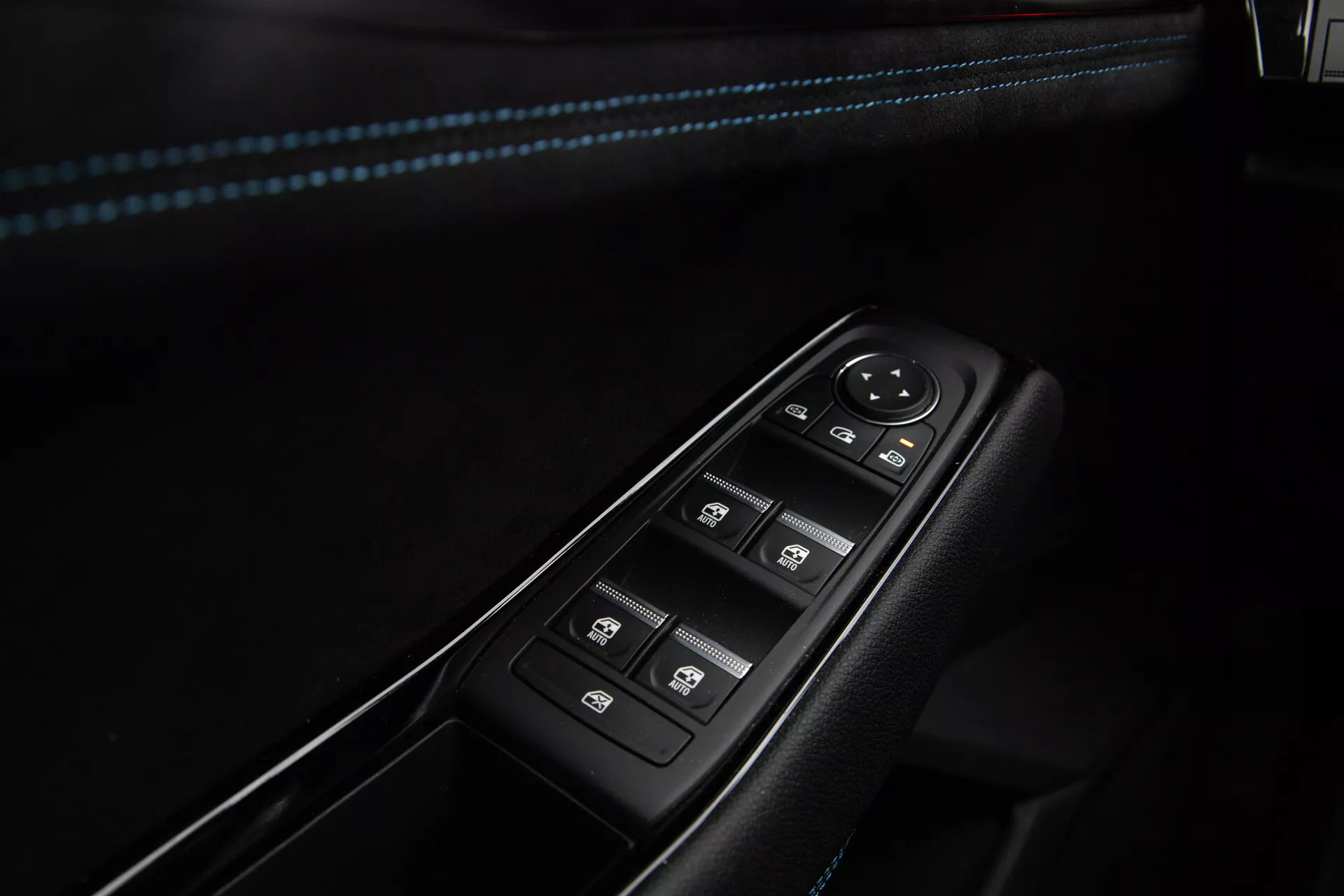 Primer plano de los controles de la puerta del lado del conductor del Renault Austral 2022 que cuenta con botones para el control eléctrico de las ventanas con función de un solo toque, dial de ajuste del espejo lateral electrónico y interruptor de bloqueo central, todo encajado en un panel negro con ribete cromado y costuras acentuadas en azul en el reposabrazos.