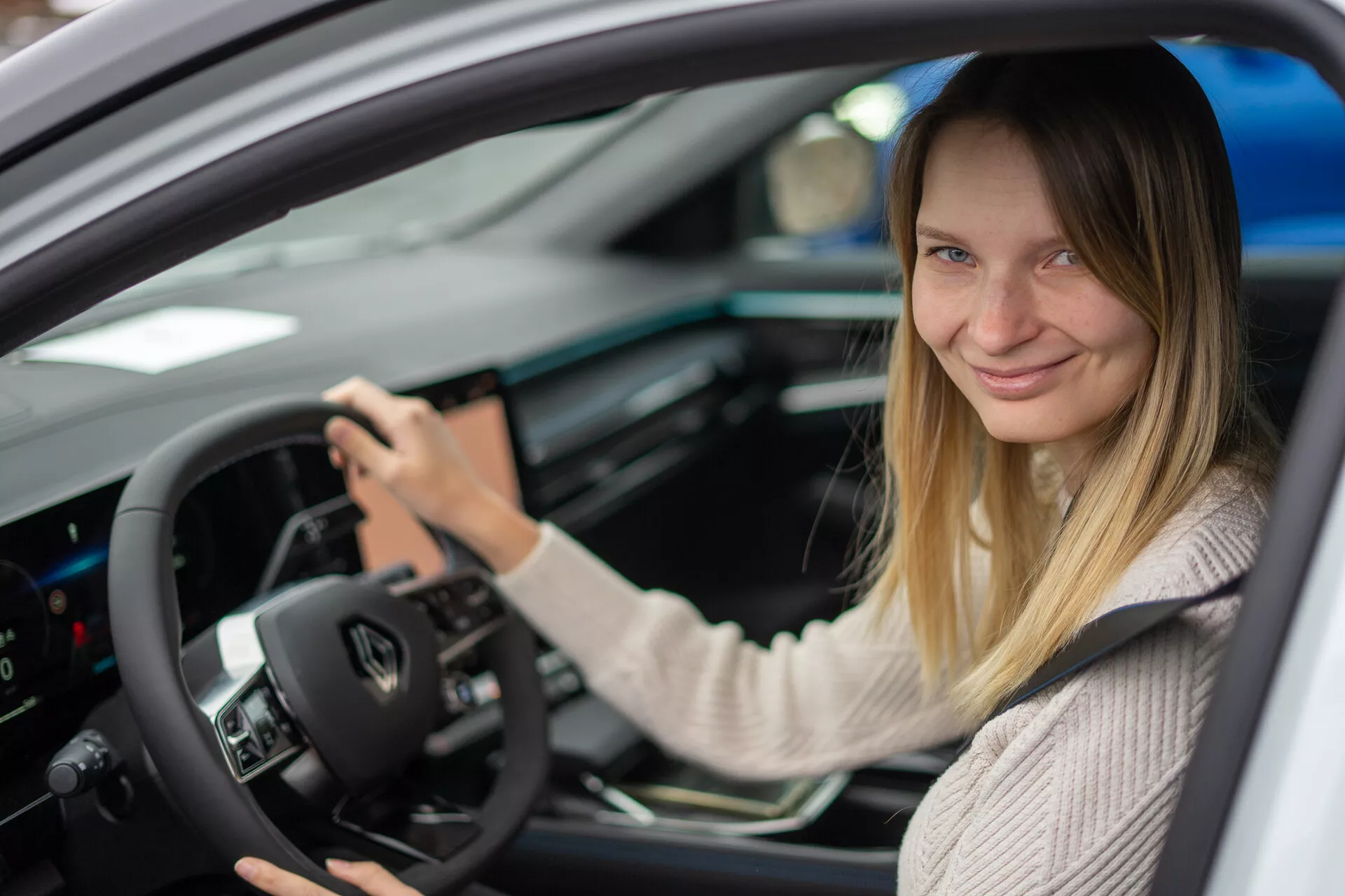 Vista interior del Renault Austral 2022 enfocada en el lado del conductor con una mujer en el asiento del conductor, con controles montados en el volante, cluster de instrumentos digitales y consola central con interfaz táctil.