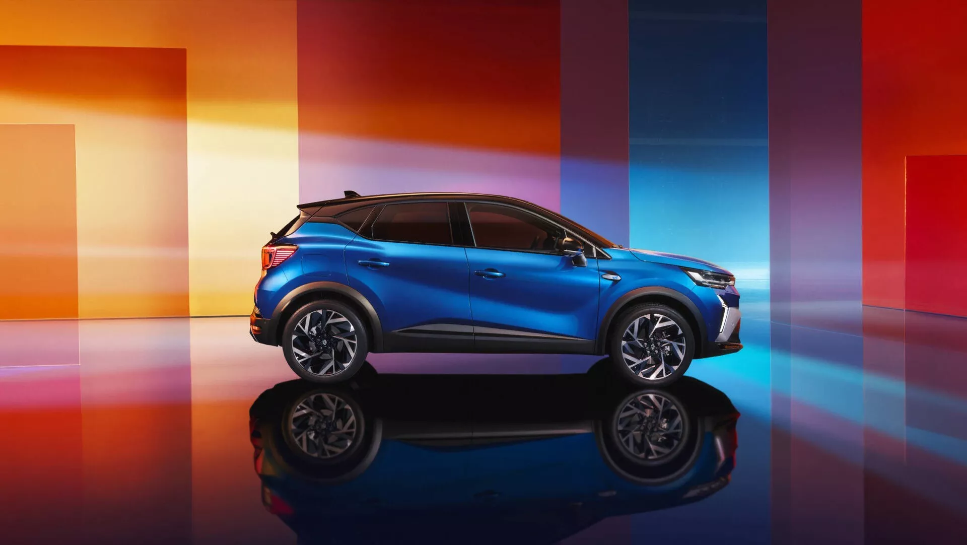Modelo 2024 de Renault Captur II facelift en azul metálico, mostrando su perfil deportivo y su elegante frontal sobre una superficie reflectante con un fondo degradado dinámico
