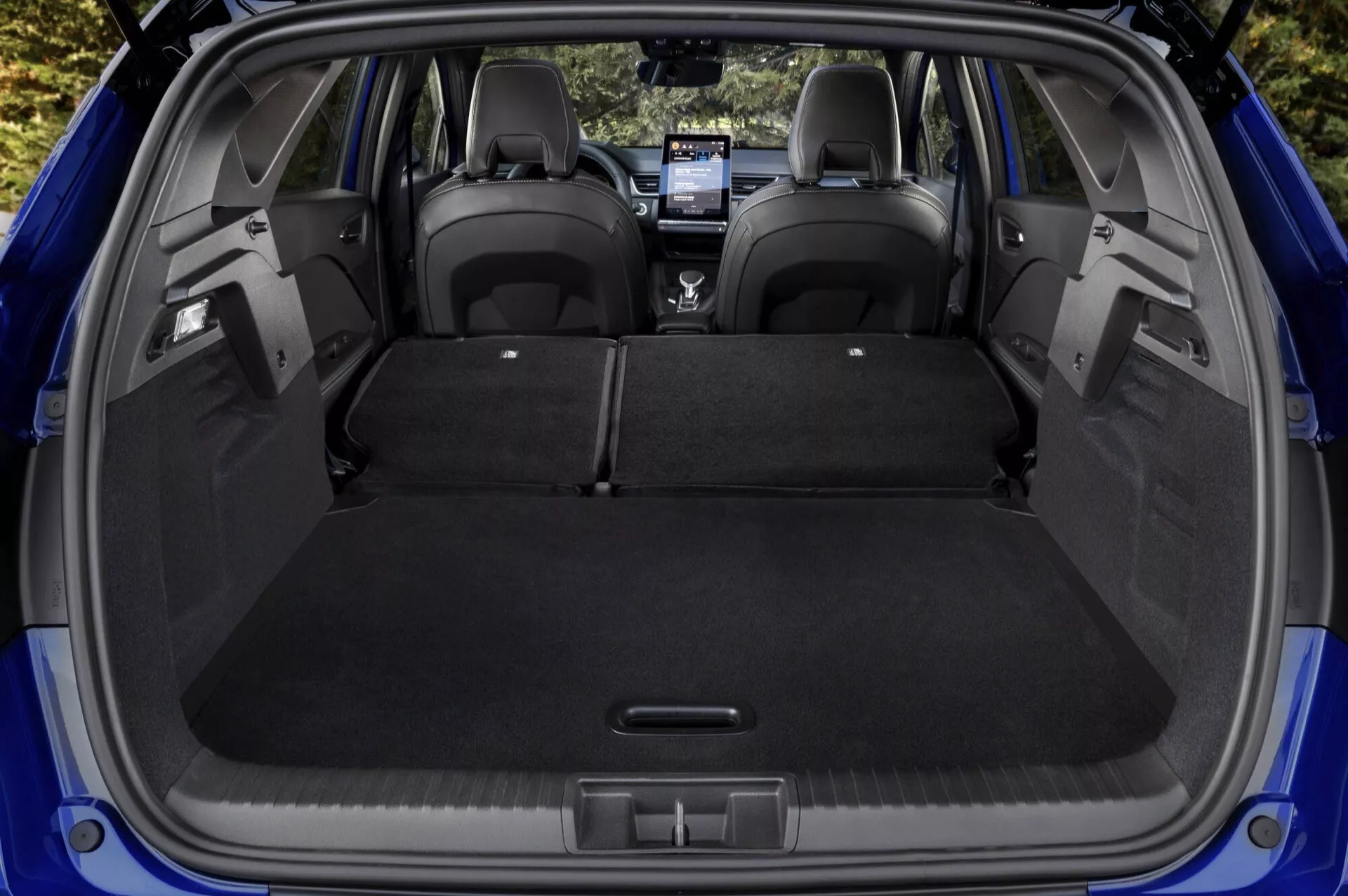 Vista del área de carga del Renault Captur II Facelift 2024 con los asientos traseros abatidos, mostrando un amplio espacio de almacenamiento, suelo de carga plano y comodidades modernas como una toma de corriente, visto desde una perspectiva trasera y ligeramente elevada.