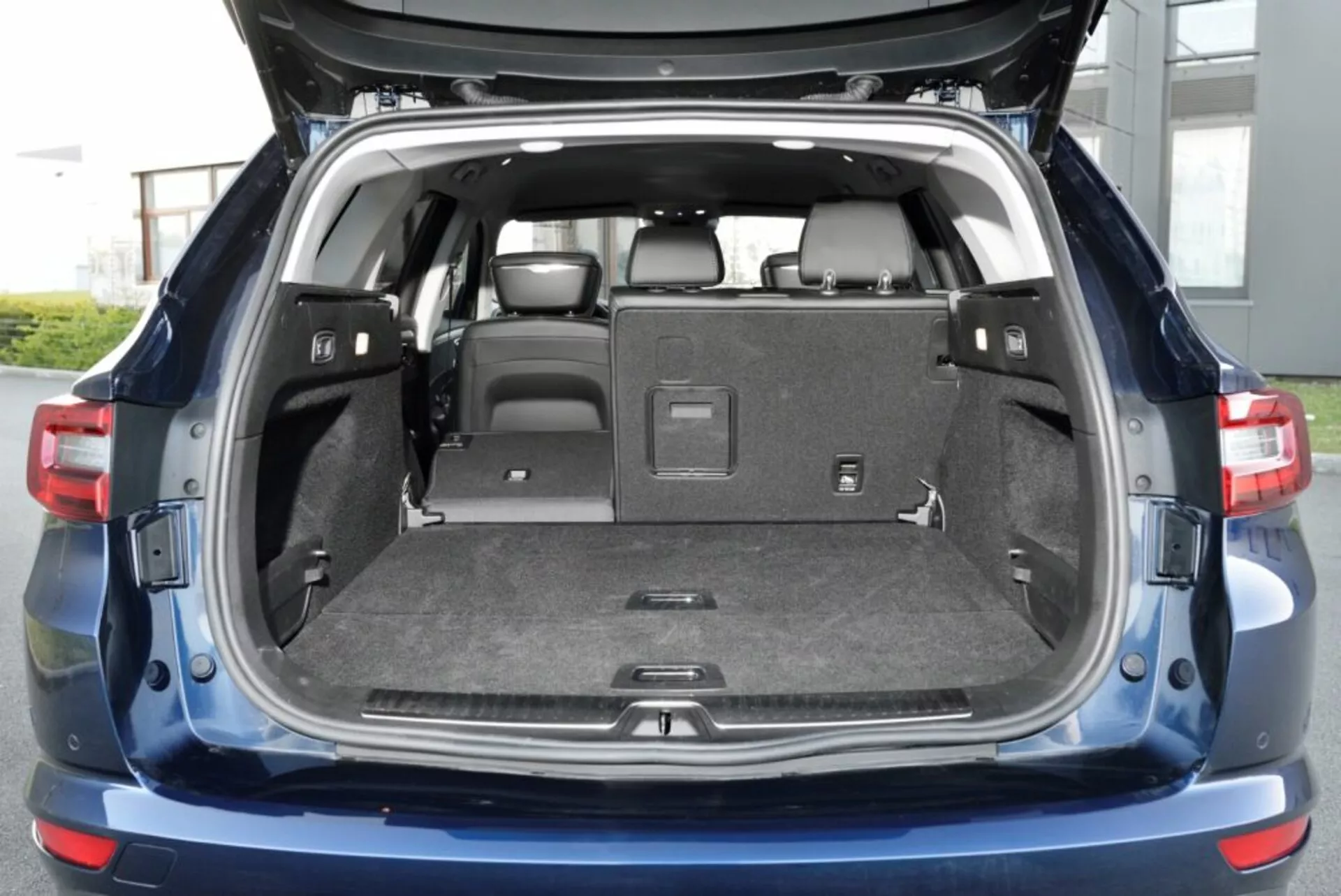 Renault Talisman Grandtour 2016 mostrando el compartimento trasero abierto con asientos traseros abatibles 60/40, amplia área de carga con iluminación interior y características de seguridad modernas incluyendo sensores en el parachoques trasero, a la luz del día con acabado azul