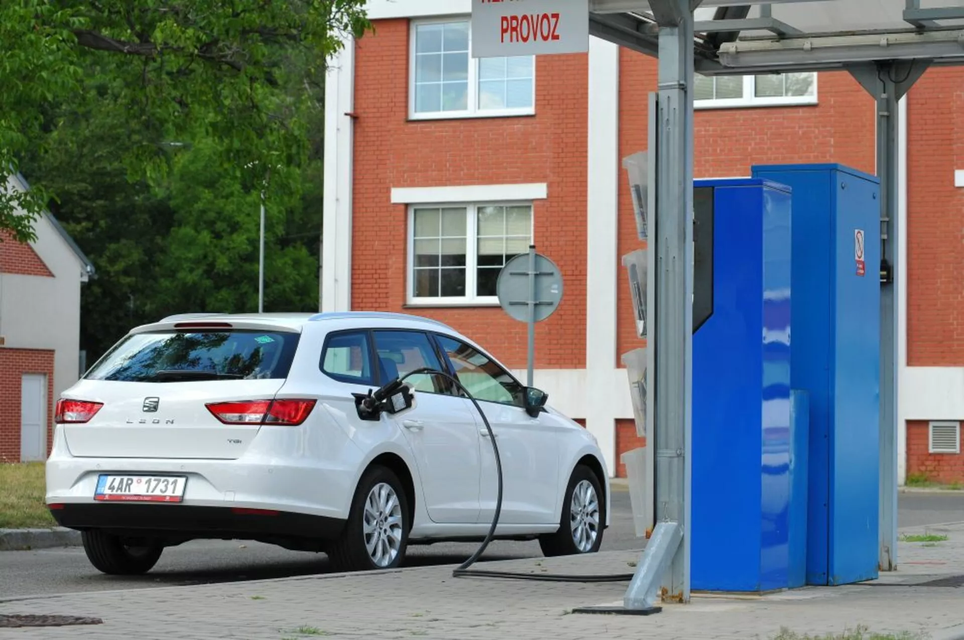 Coche hatchback Seat Leon SC blanco del 2016, eléctrico o híbrido enchufable, aparcado en una estación de carga para vehículos eléctricos, mostrando una vista trasera de tres cuartos que destaca las luces traseras, el parabrisas trasero, el perfil del maletero y el puerto de carga en el lado derecho