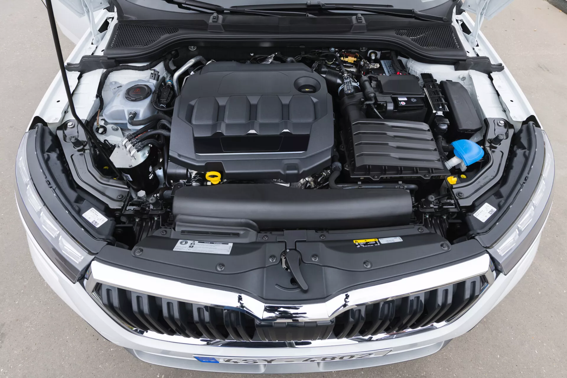 Vista detallada del compartimento del motor abierto de Skoda Kamiq 2019 que muestra la cubierta del motor, protecciones de plástico, depósitos de fluidos y conductos electrónicos sin elementos de diseño exterior visibles