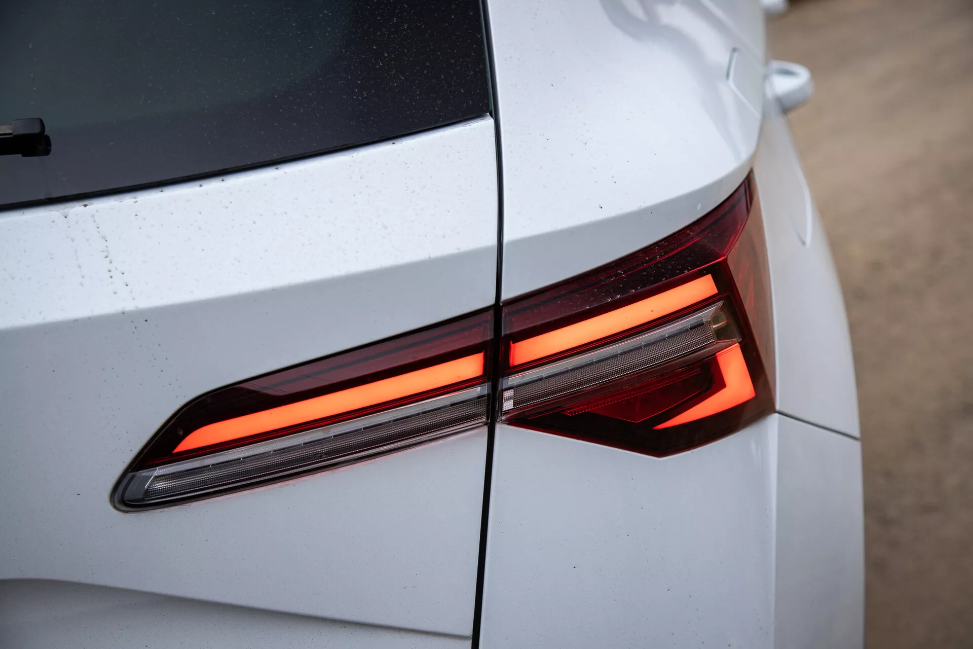 Primer plano de la sección trasera del Skoda Karoq 2021 mostrando el diseño moderno de la luz trasera LED, con énfasis en las líneas angulares y el cuerpo del coche de color claro y brillante con gotas de agua visibles