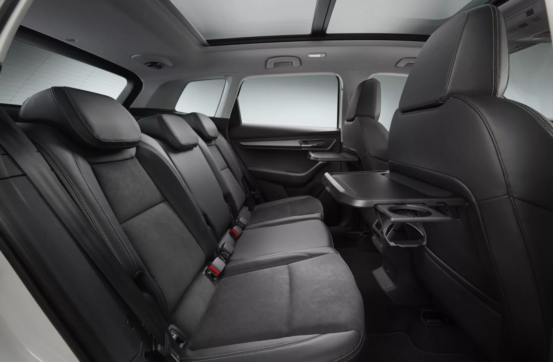Vista interior de un Skoda Karoq 2017 enfocado en el área de asientos de la segunda fila con asientos de cuero negro premium, reposabrazos abatible con porta vasos, panel de puerta con controles eléctricos, bolsillos de almacenamiento detrás de los asientos delanteros, cinturones de seguridad para todas las posiciones y una consola central que se extiende a la segunda fila, todo bajo iluminación de estudio realzada