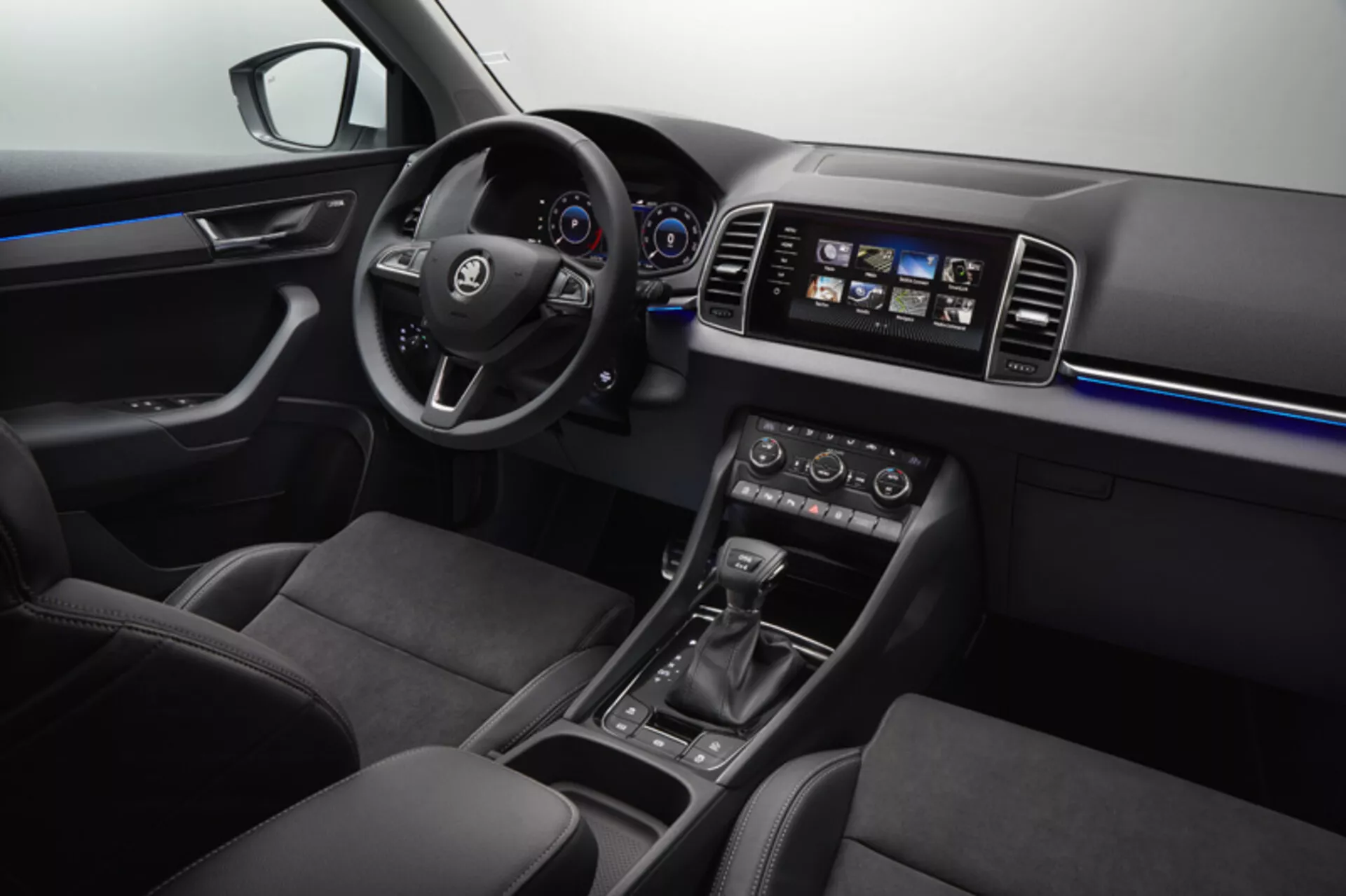 Vista interior del Skoda Karoq 2017 mostrando el tablero, puerta del conductor con controles de ventanas y espejos, volante con botones de multimedia y control de crucero, cuadro de instrumentos digital-analógico, sistema de infoentretenimiento táctil, control de clima de zona dual, selector de cambio automático, selección de modo de conducción y asientos tapizados en cuero