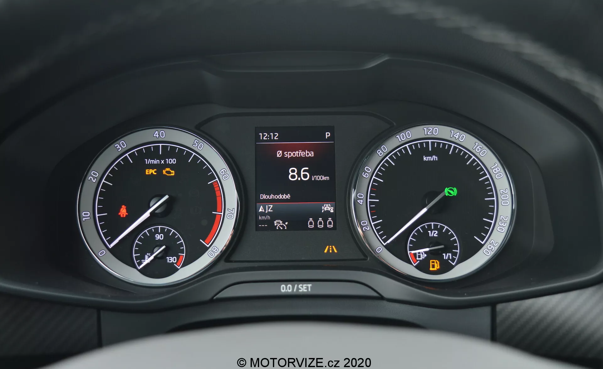 Fotografía en primer plano desde la perspectiva del conductor del panel de instrumentos del Skoda Kodiaq 2017 que muestra una combinación de indicadores analógicos y digitales detrás del volante. El tablero incluye un tacómetro con una luz de advertencia naranja, una pantalla central que muestra diversa información del vehículo como la hora, el estado del freno de estacionamiento, el modo deportivo, el alcance y la temperatura, y un velocímetro con indicador de combustible y de arranque/parada automática.