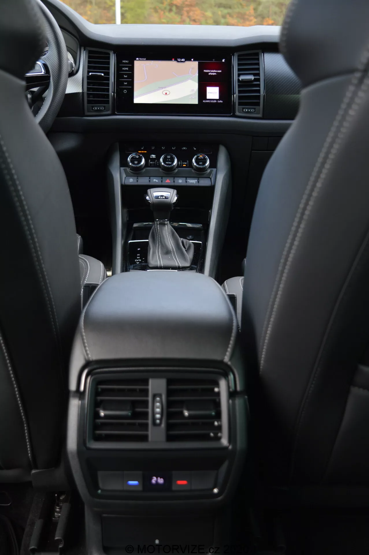 Interior del coche Skoda Kodiaq 2017, mostrando el tablero delantero desde la perspectiva del asiento trasero. La imagen resalta los asientos de cuero, consola central con palanca de cambios automática, botones de control, sistema de infoentretenimiento con pantalla táctil mostrando un mapa de navegación, ventilaciones del control de clima y una vista parcial del panel de instrumentos mostrando detalles operativos críticos.