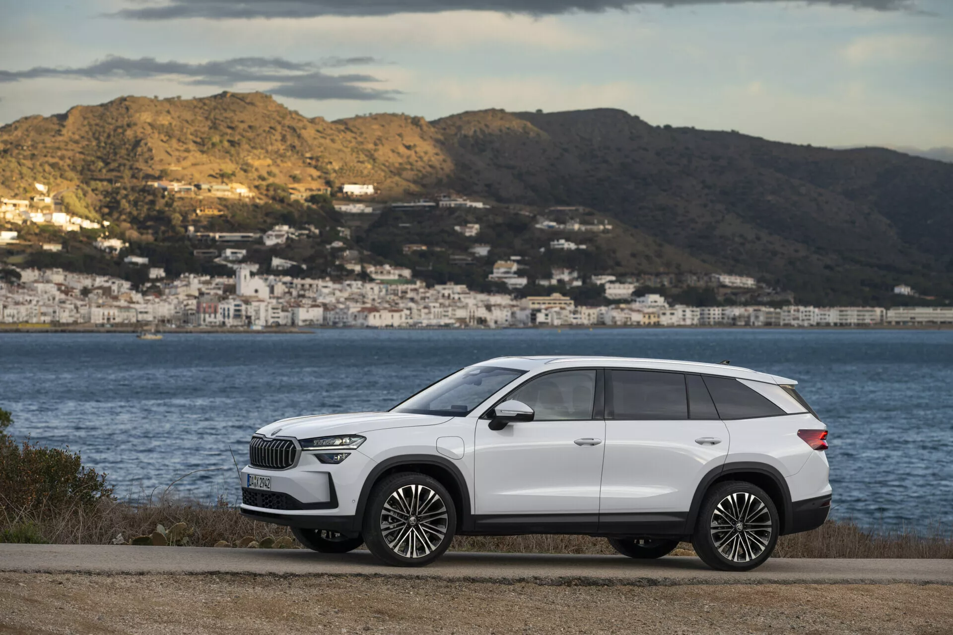 SUV premium Skoda Kodiaq blanco 2024 aparcado en una carretera plana con paisaje costero al fondo, mostrando el elegante perfil lateral del vehículo con detalles cromados y grandes llantas de aleación