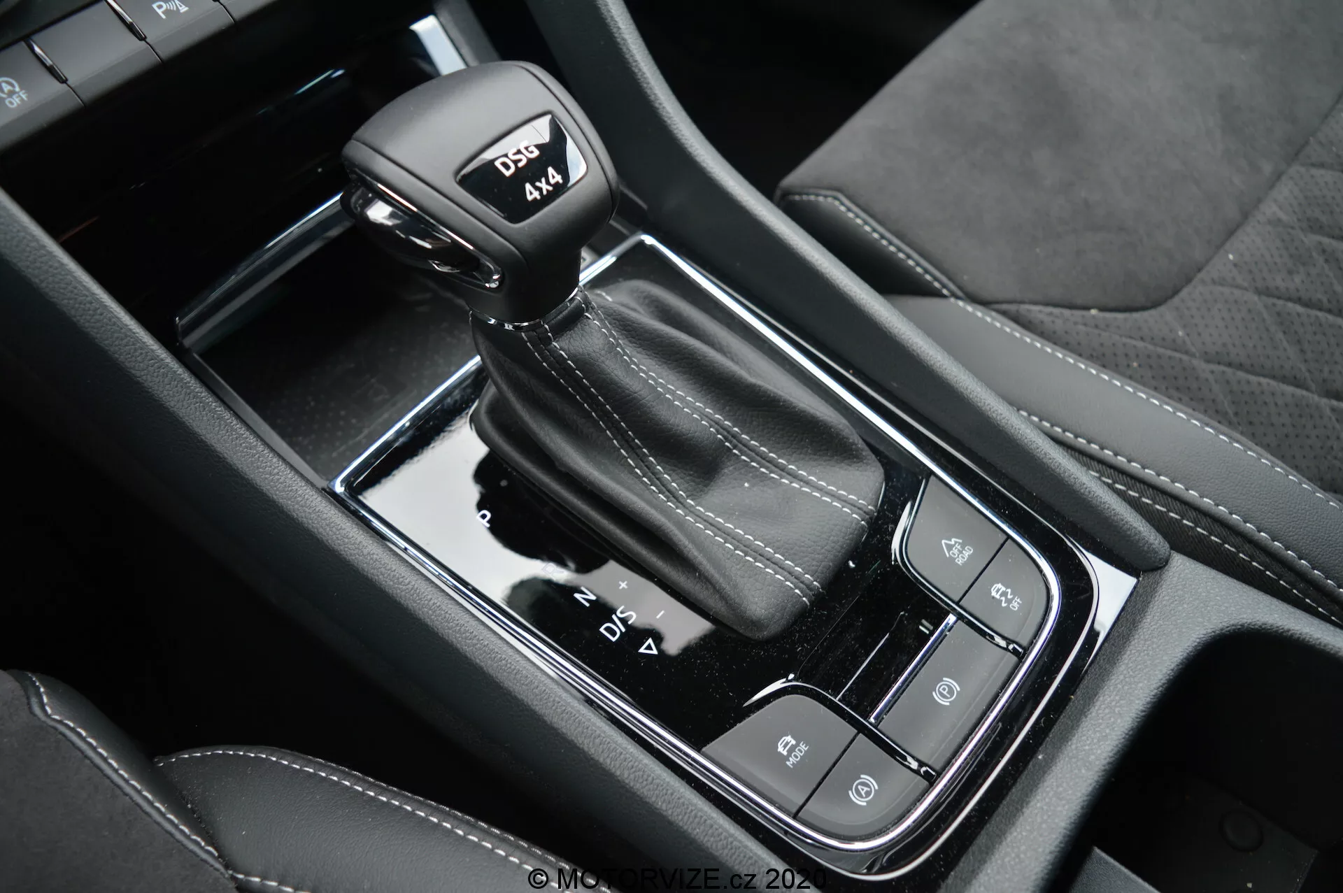 Vista detallada de la palanca de cambios automática y la consola central negra brillante del Skoda Kodiaq 2017, que presenta modos de conducción, freno de mano electrónico y botón de auto-hold; destaca las costuras de cuero en la palanca con modo deportivo.