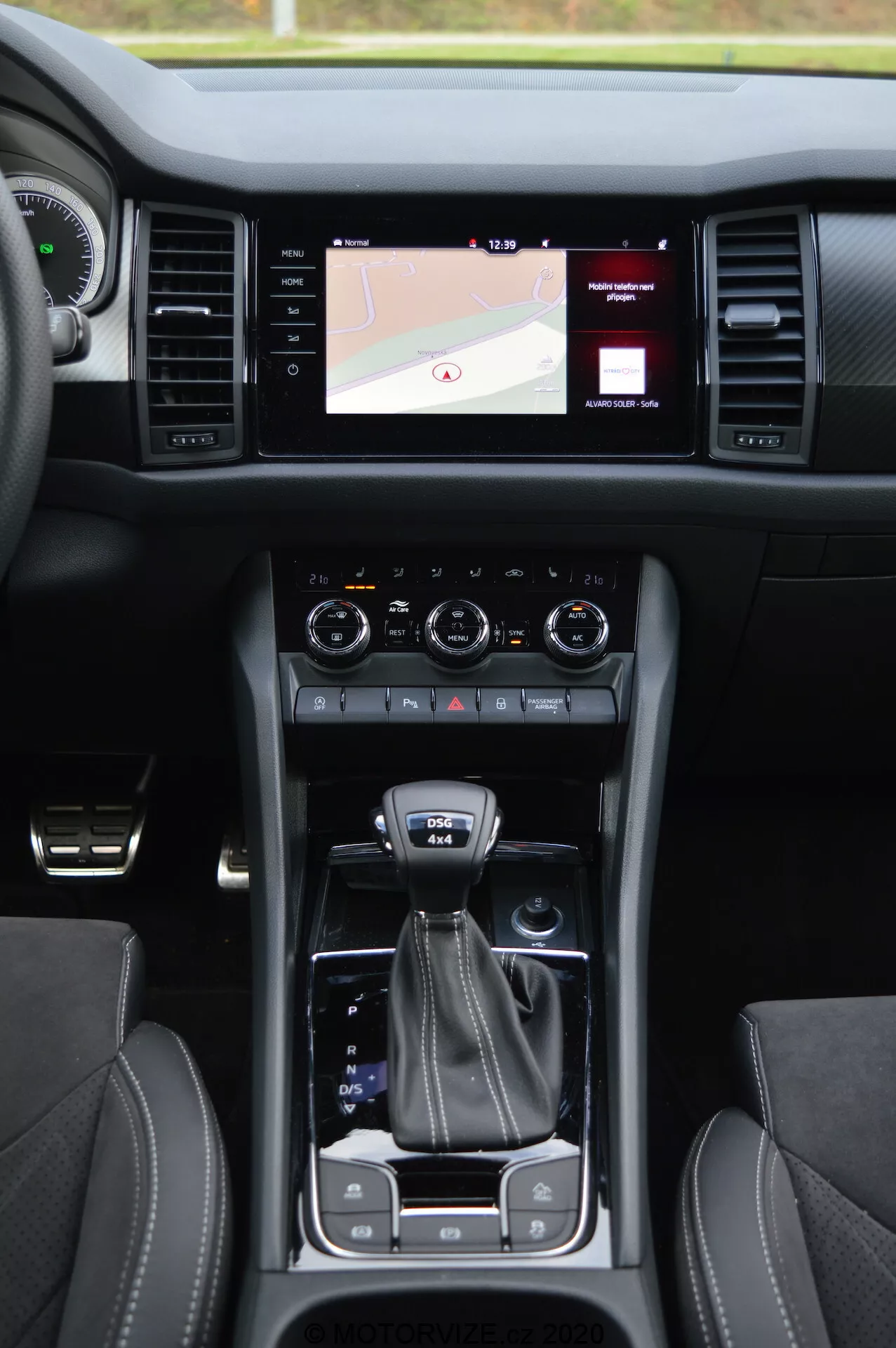 Vista interior de un Skoda Kodiaq 2017 que muestra la consola central, el sistema de infoentretenimiento con pantalla táctil mostrando un mapa, diales de control de clima duales, palanca de cambios, selector de modo de conducción, portavasos, asientos de cuero con costuras en contraste y botón de encendido sin llave