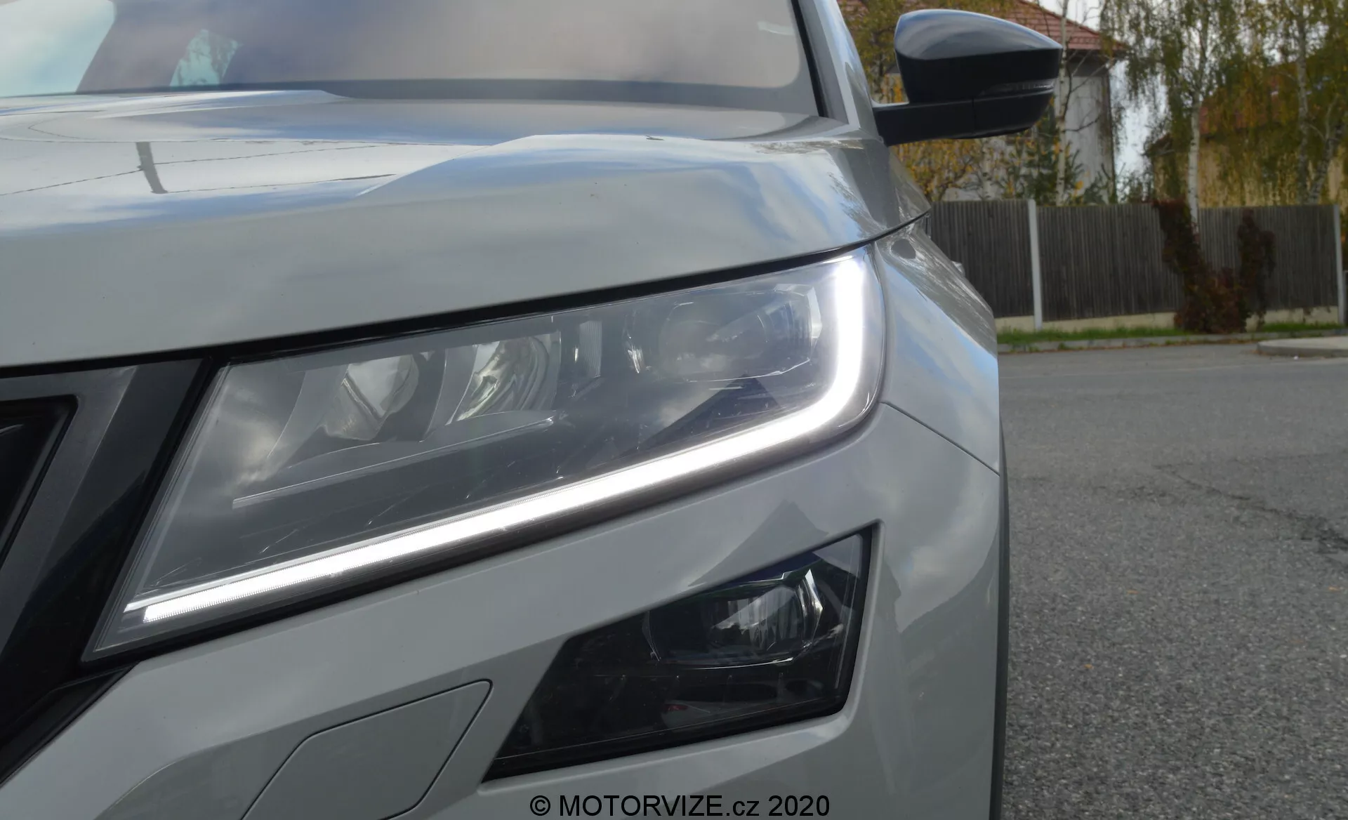 Vista en primer plano del lado delantero izquierdo de un Skoda Kodiaq 2017. La perspectiva de bajo ángulo resalta las luces diurnas LED distintivas y los faros principales detallados que sugieren tecnología de iluminación avanzada. Debajo del faro principal se ven las luces antiniebla de diseño moderno. La imagen también muestra parte de la parrilla frontal, una pintura metálica con líneas de carrocería nítidas y un espejo lateral con indicador de señal integrado. Hay una marca de agua 'MOTORVIZE.cz 2020' que indica la fuente de la fotografía.