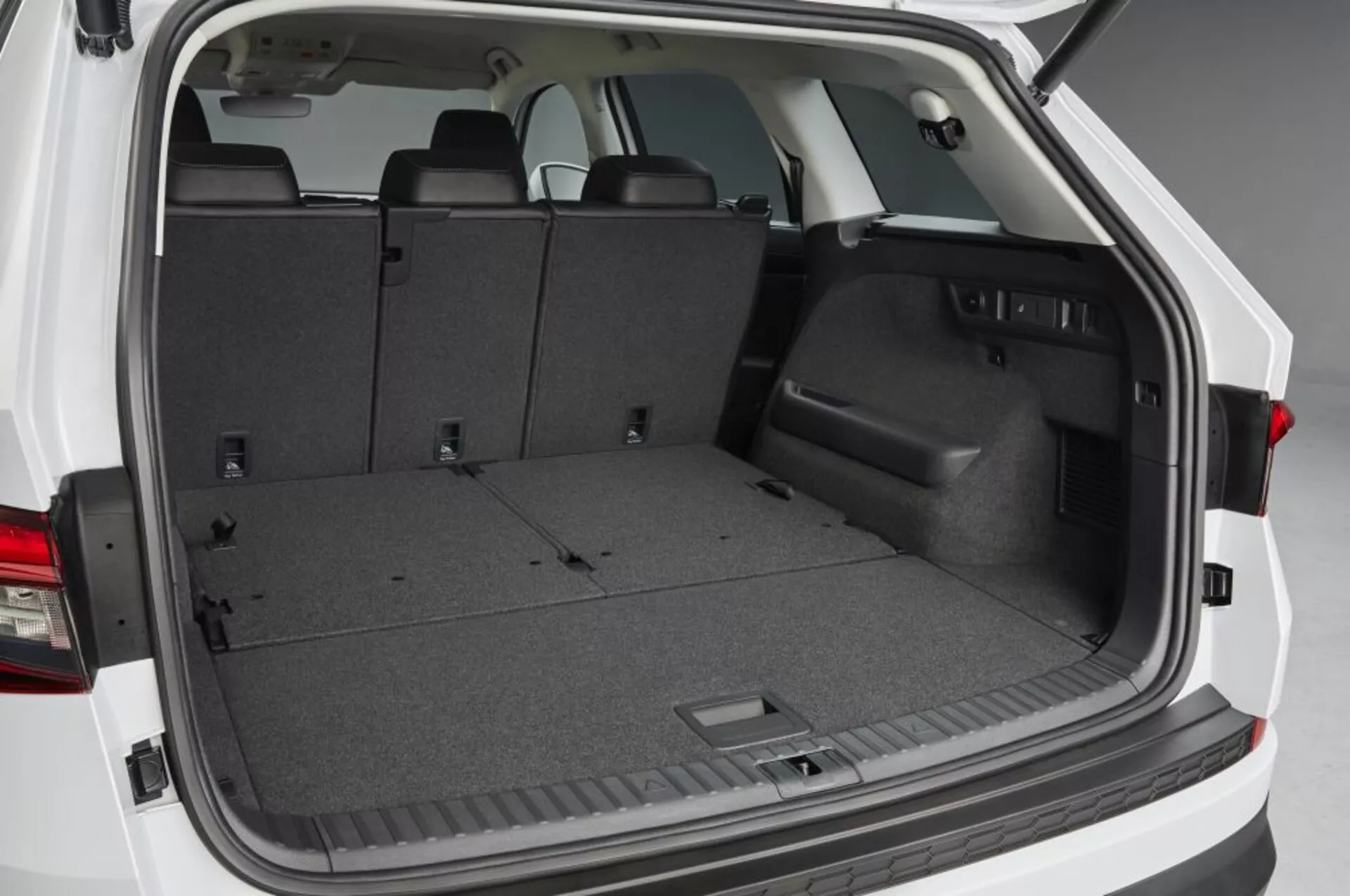 Vista del espacio de carga trasero del Skoda Kodiaq 2017 con portón trasero abierto, mostrando un área de carga alfombrada vacía, asientos traseros plegables para ampliar espacio, borde de plástico lateral con compartimiento de almacenamiento empotrado, puntos de amarre y iluminación interior, resaltando soluciones prácticas de almacenamiento y gestión de carga.