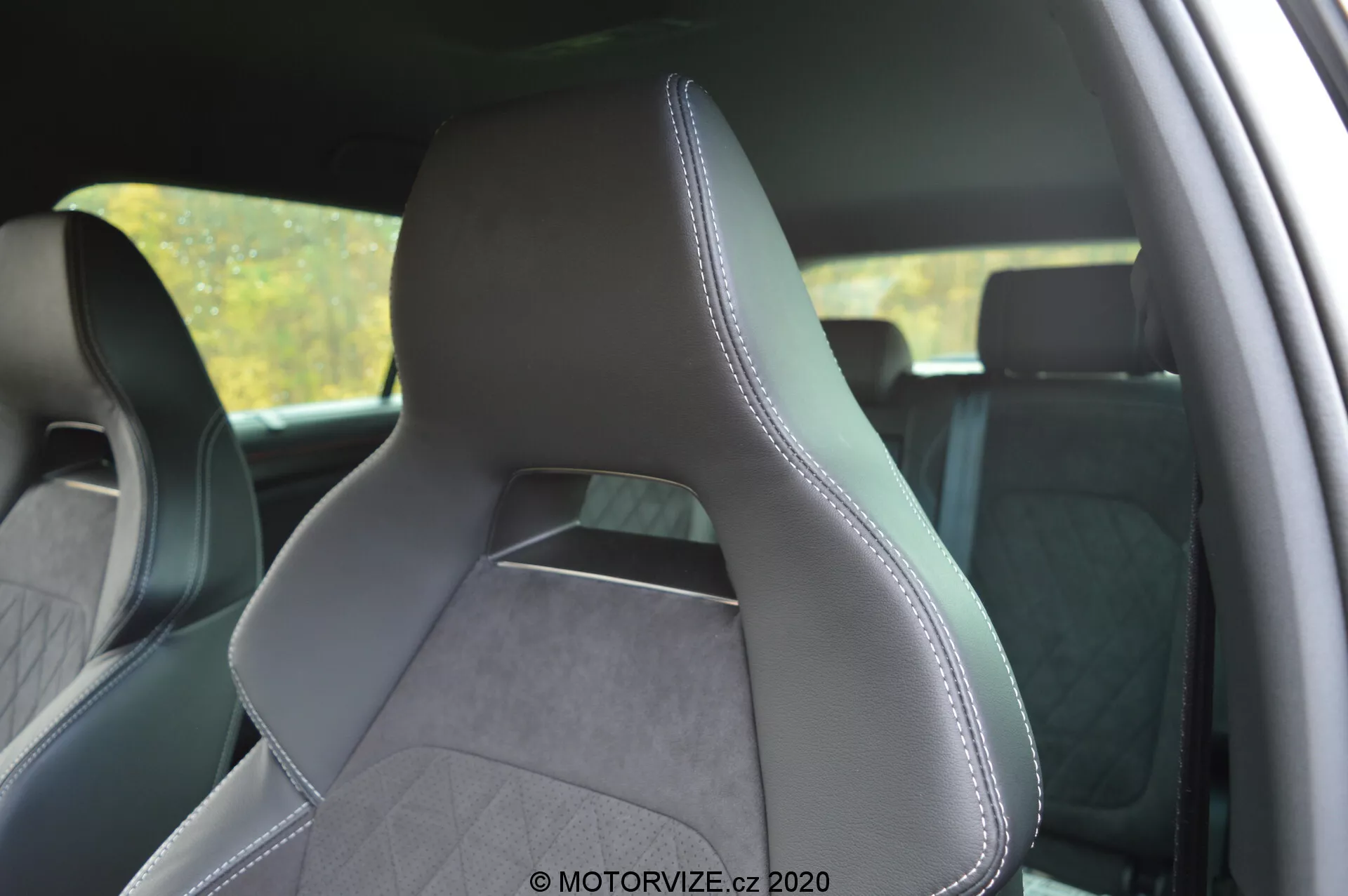 Interior del Škoda Kodiaq 2017 centrado en el asiento del conductor desde una perspectiva lateral trasera, destacando la tapicería de cuero y tela texturizada con costuras precisas a lo largo de los bordes. El asiento de diseño moderno y deportivo cuenta con refuerzos laterales pronunciados para un mayor soporte, reposacabezas integrado y un patrón de costura en diamante que sugiere una estética premium. El fondo del interior está ligeramente borroso para enfatizar el asiento.