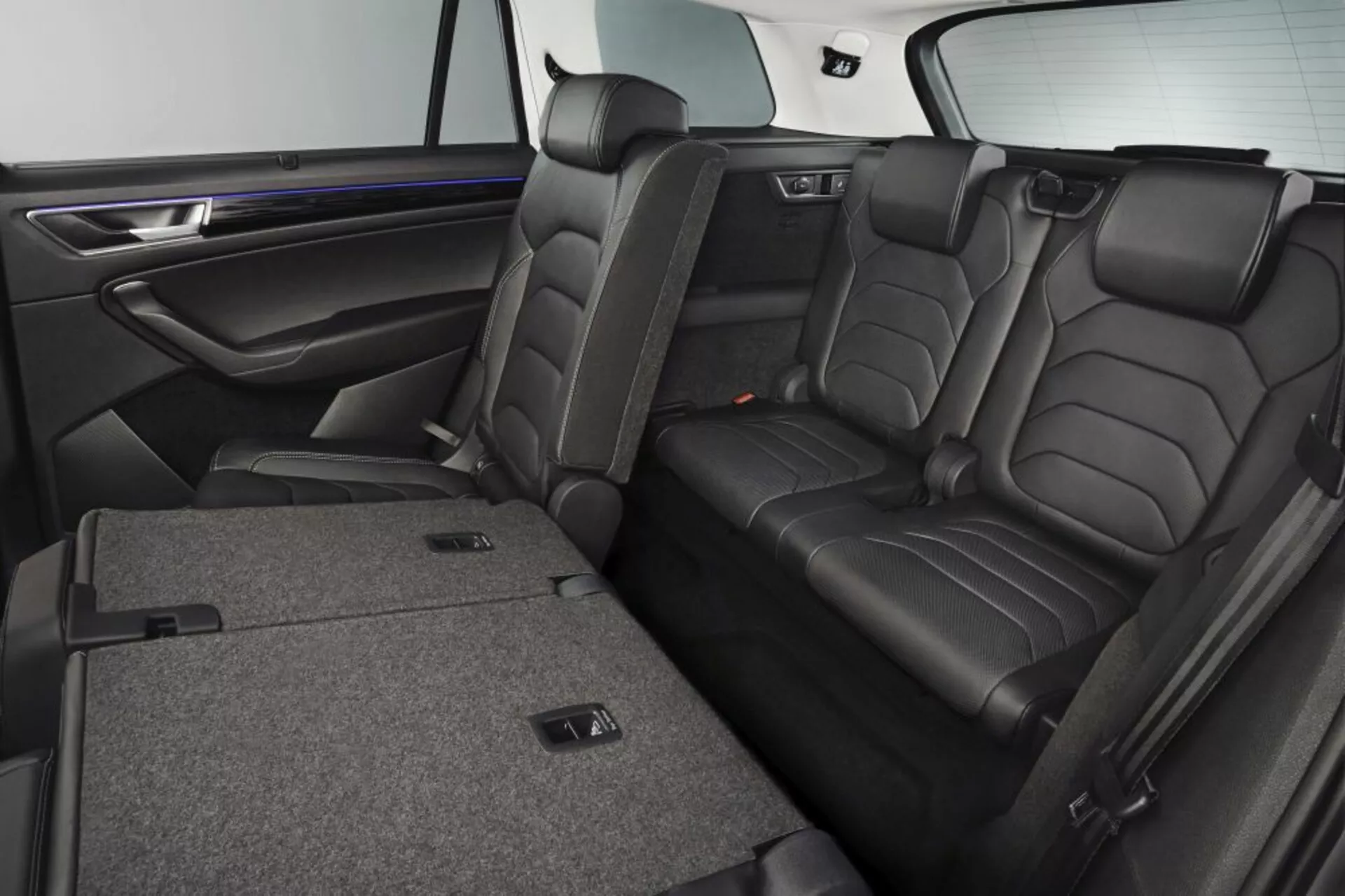 Interior del Skoda Kodiaq 2017 mostrando asientos traseros de cuero de lujo con reposacabezas, función de plegado dividido 60/40 para ampliar el espacio de carga, reposabrazos central con portavasos, y recubrimiento de puerta de efecto madera premium con iluminación ambiental