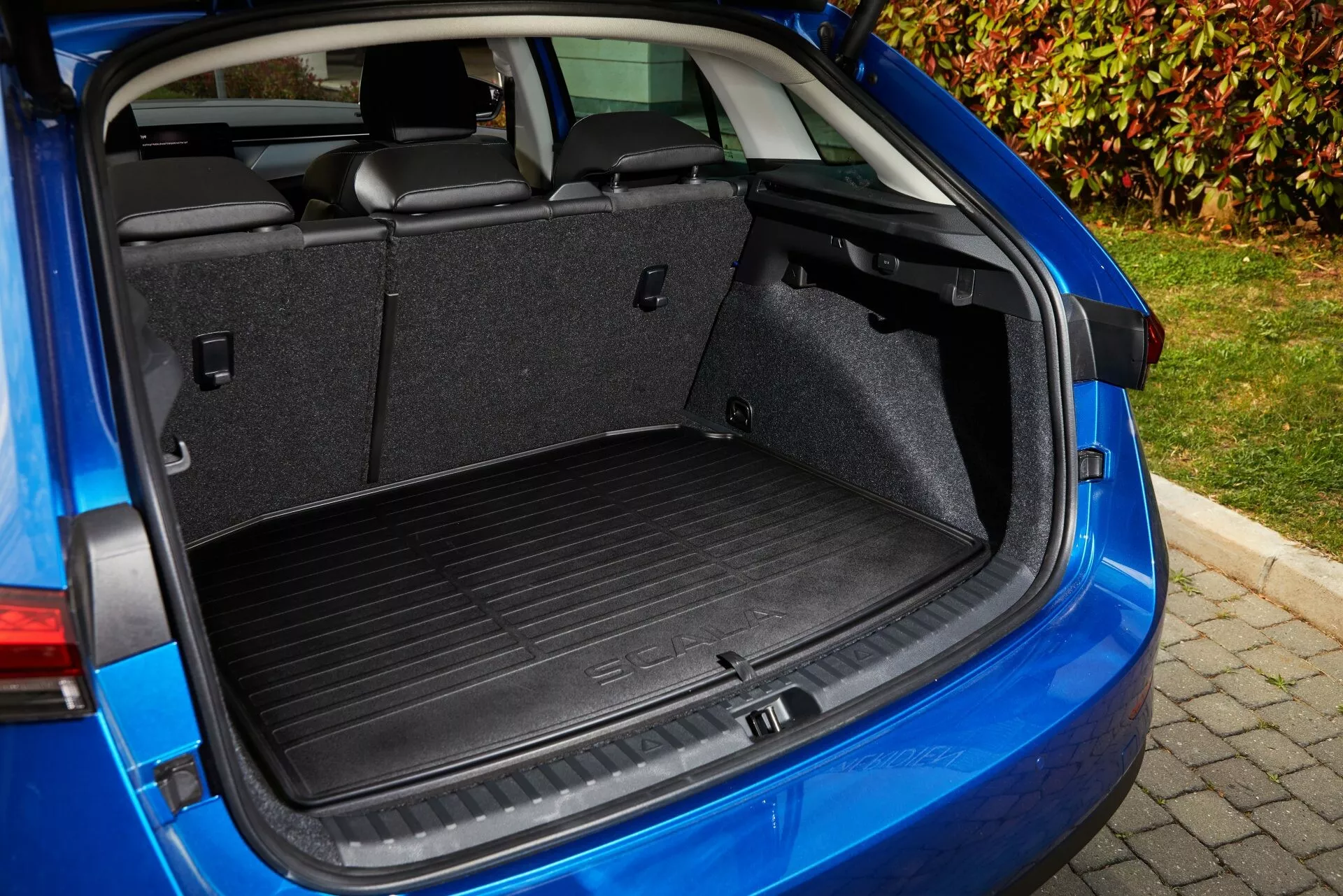 Área de carga del Skoda Scala 2019 desde un ángulo trasero de tres cuartos, destacando el espacio del maletero, mecanismo de portón trasero, revestimiento interior y características de utilidad que incluyen asiento trasero divisible 60/40, ganchos para el equipaje y un enchufe de 12V