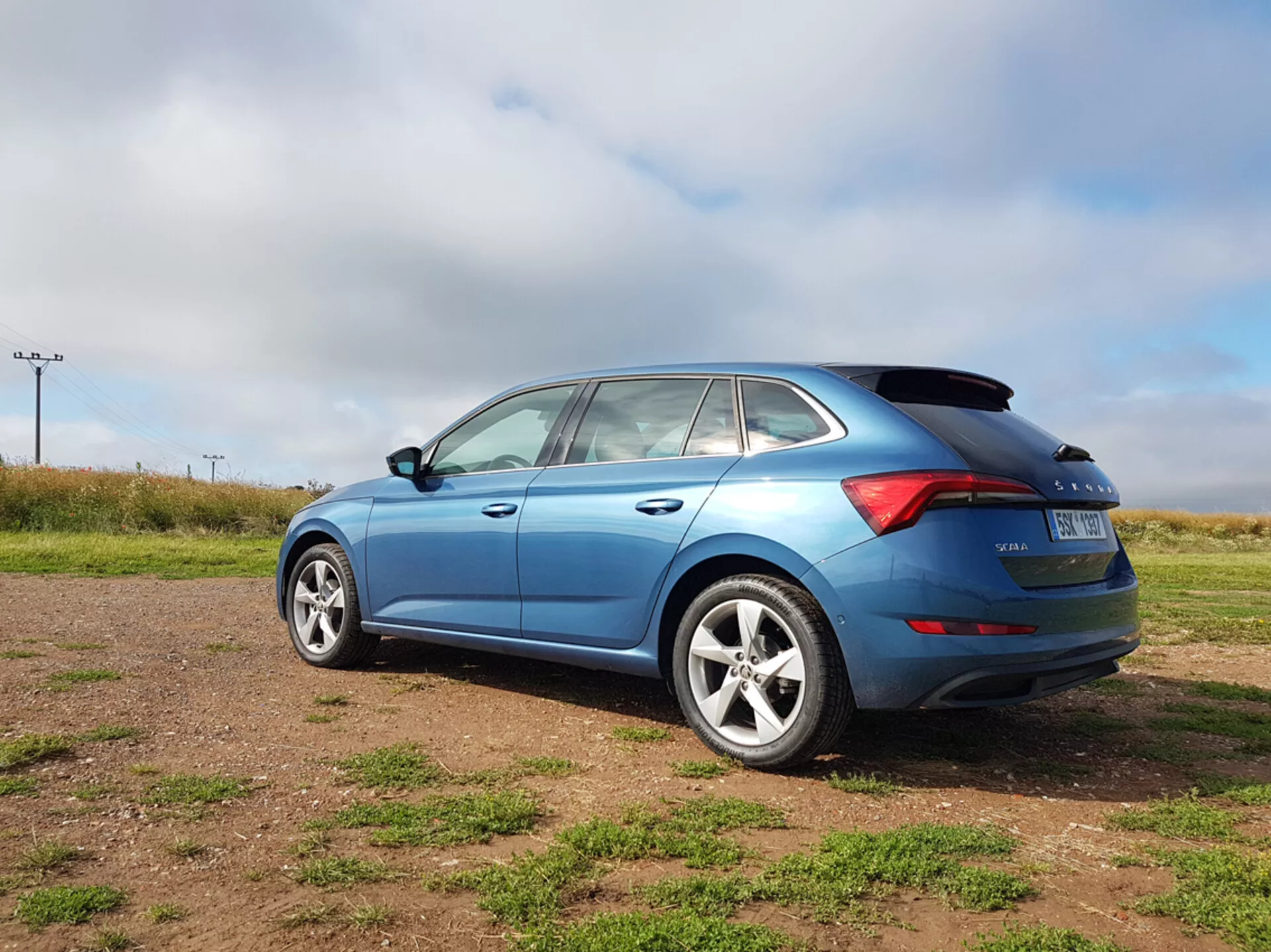 Hatchback azul Skoda Scala 2019 mostrando elementos de diseño lateral y trasero, incluida la forma de las ventanas, las luces traseras LED y las ruedas de aleación, fotografiado desde un ángulo trasero de tres cuartos en un terreno herboso