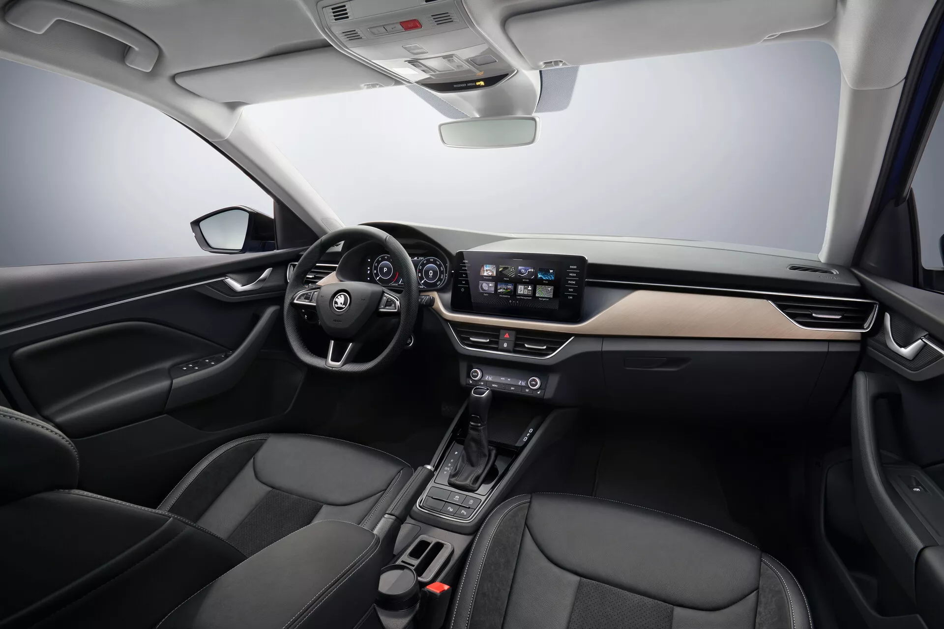Vista interior del Skoda Scala 2019 mostrando las áreas del conductor y pasajero, con volante a la izquierda con controles integrados, tablero moderno con acentos de metal cepillado, cluster de instrumentos digital detrás del volante, sistema de infoentretenimiento con pantalla táctil de 8 pulgadas, consola central minimalista con selector de cambios automático, asientos acentuados en cuero negro y tecnología avanzada del vehículo incluyendo control automático del clima y características de conectividad, bajo una iluminación de estudio suave que enfatiza la disposición espaciosa y el diseño ergonómico del coche.