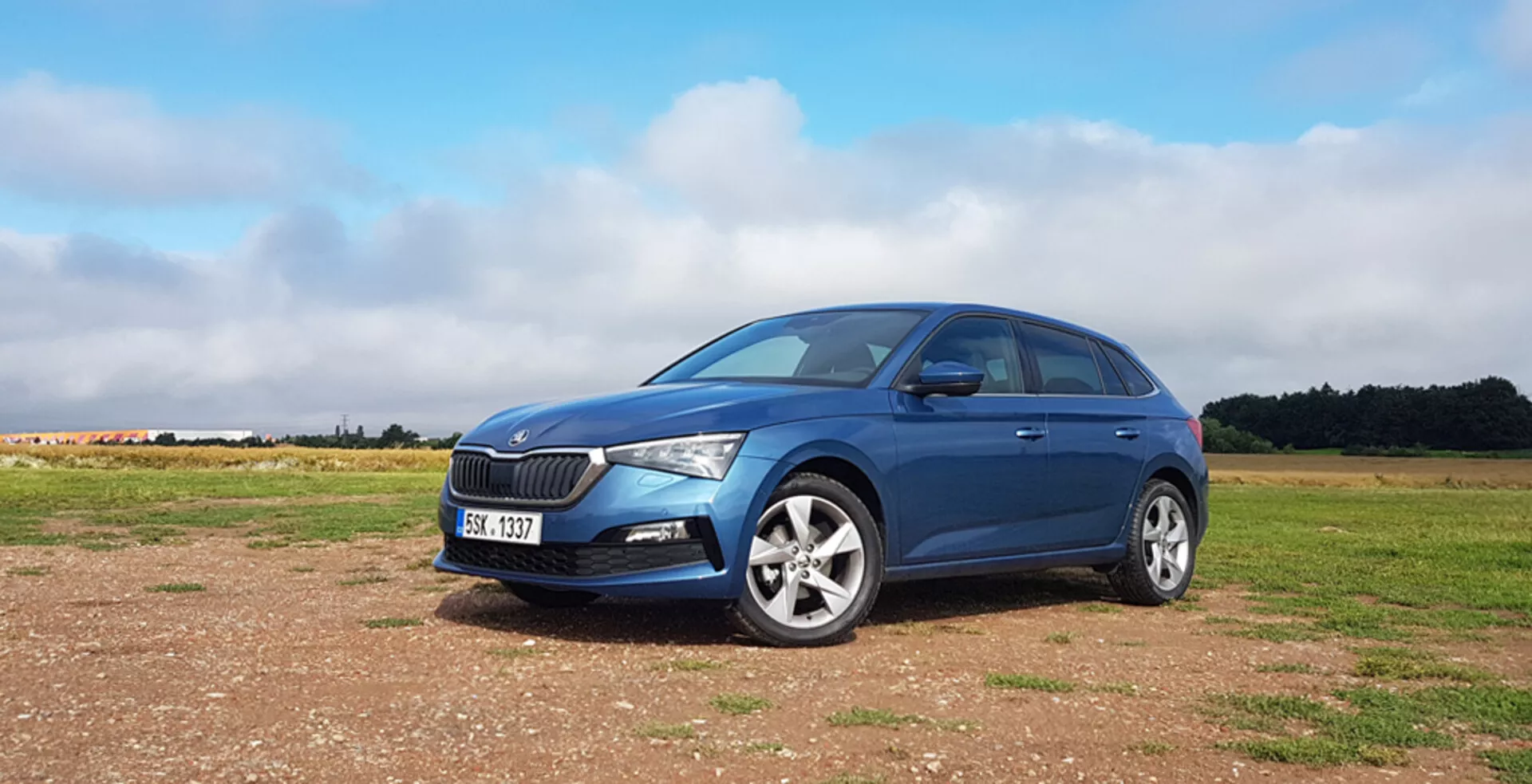 Hatchback azul Skoda Scala 2019 sobre superficie sin pavimentar con rejilla frontal distintiva, faros delanteros LED modernos, rines de aleación y un elegante perfil lateral izquierdo contra un fondo de cielo parcialmente nublado